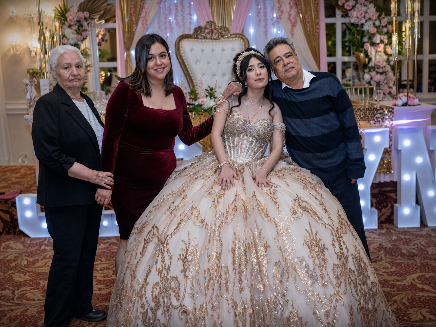 Family posing with a quinceañera girl in an ornate gold ballgown at an elegant celebration venue.