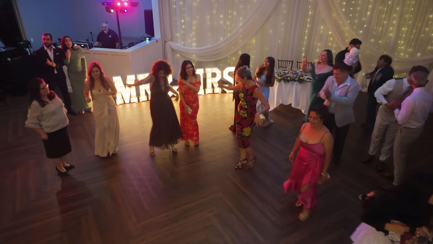 Guests dancing at a wedding reception with MR & MRS marquee letters glowing on the dance floor.