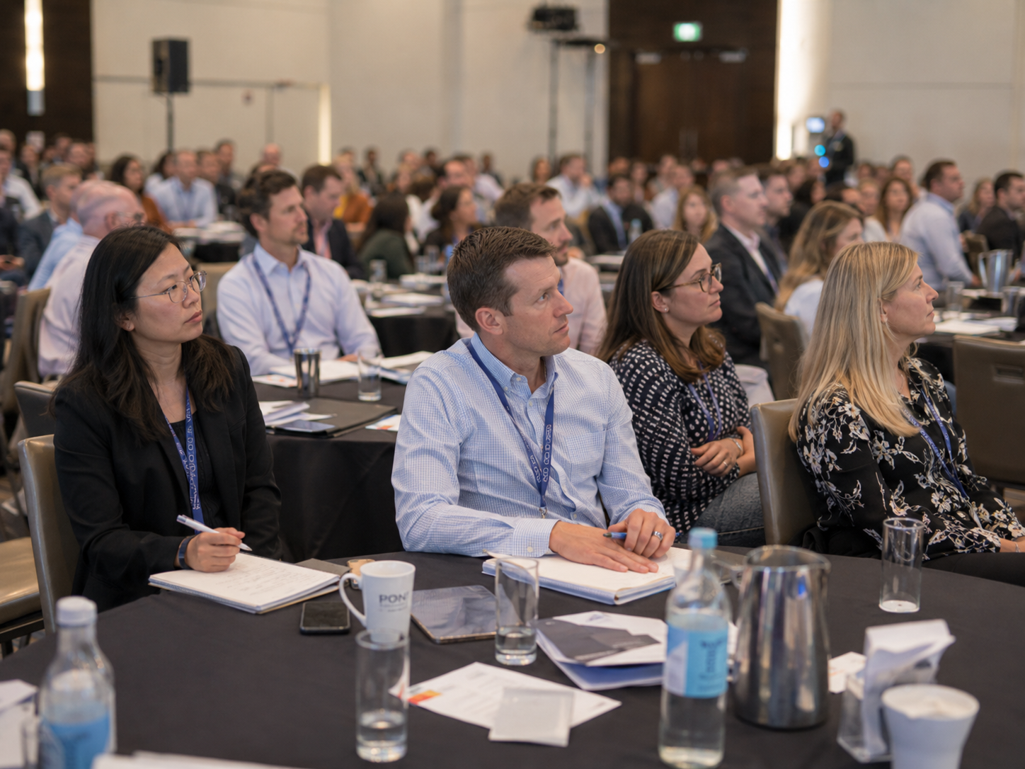 Business professionals attending a corporate conference seated at tables in a large hotel ballroom.