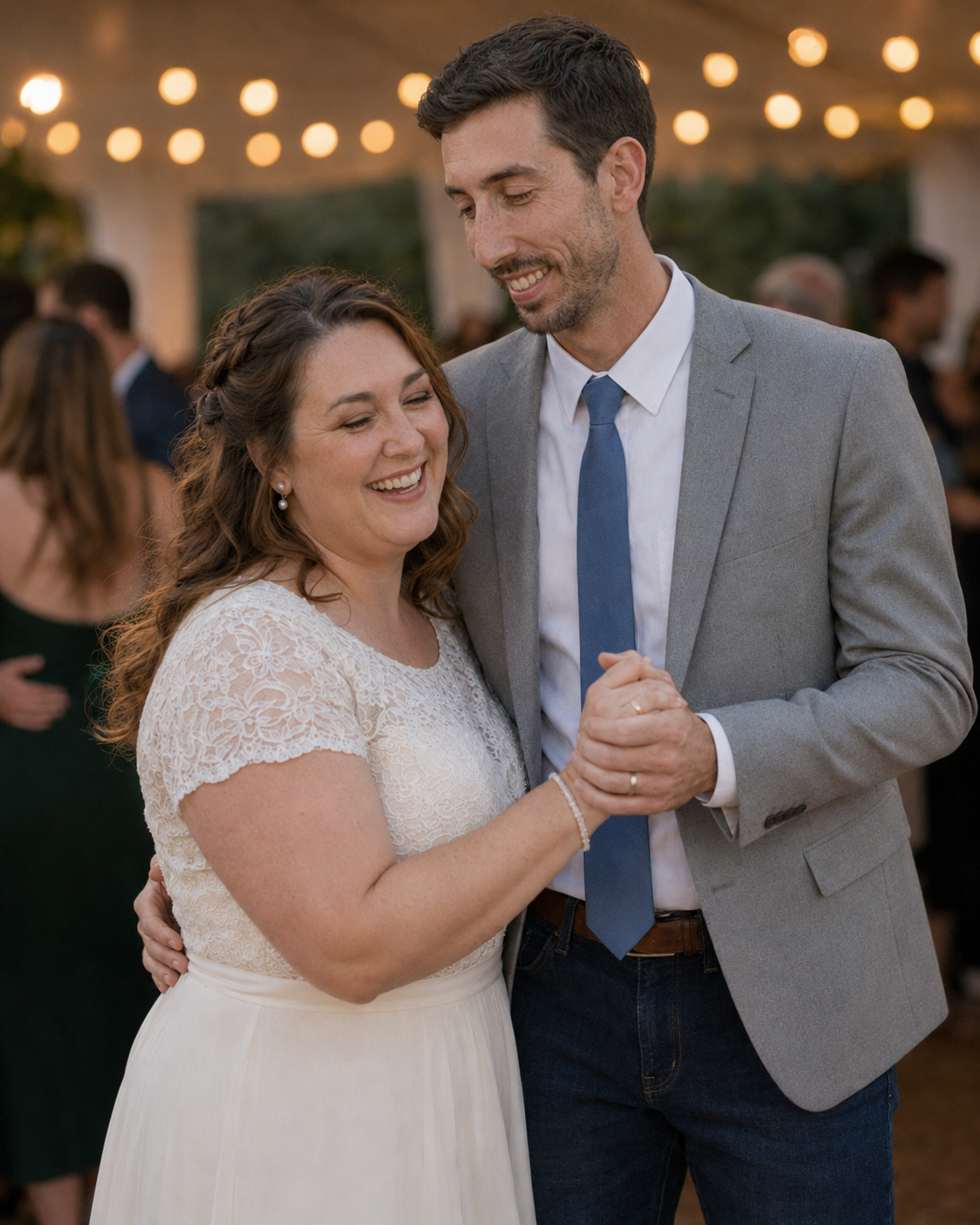 Bride and groom sharing a joyful first dance under string lights at their wedding reception.