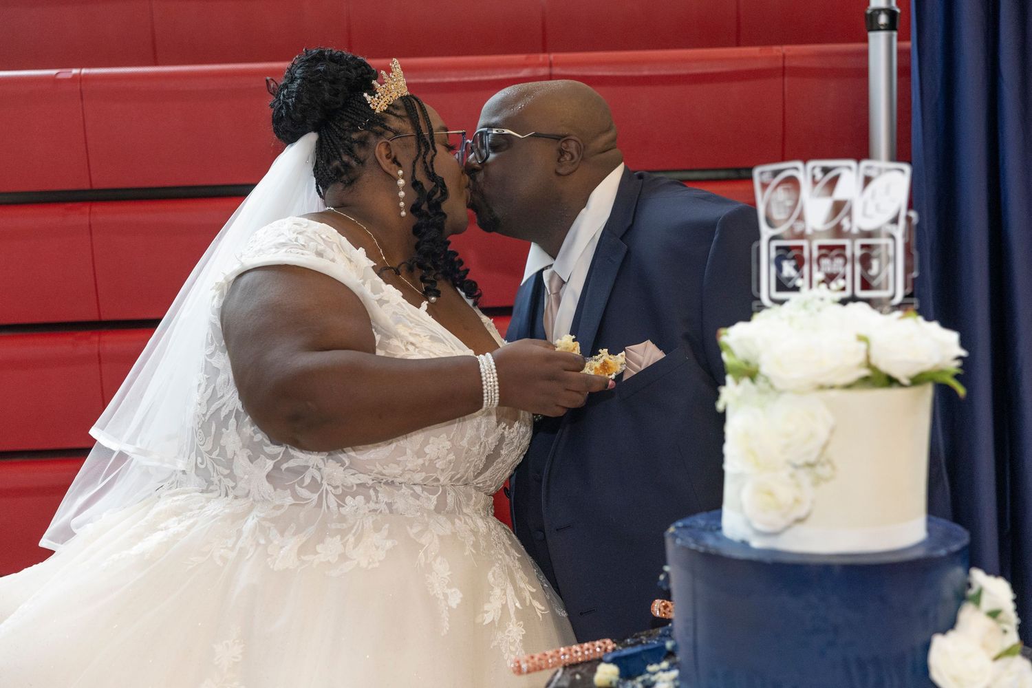 Bride and groom share a kiss beside a navy blue wedding cake at their reception ceremony.