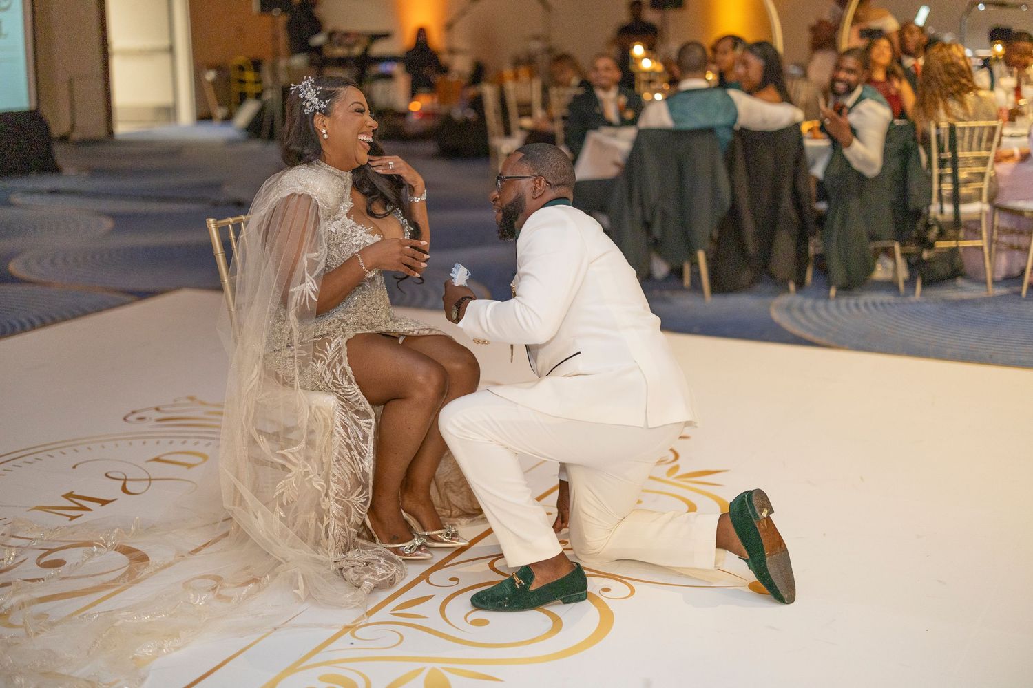 Couple in white attire performs a traditional wedding dance on a decorated white floor at their reception.