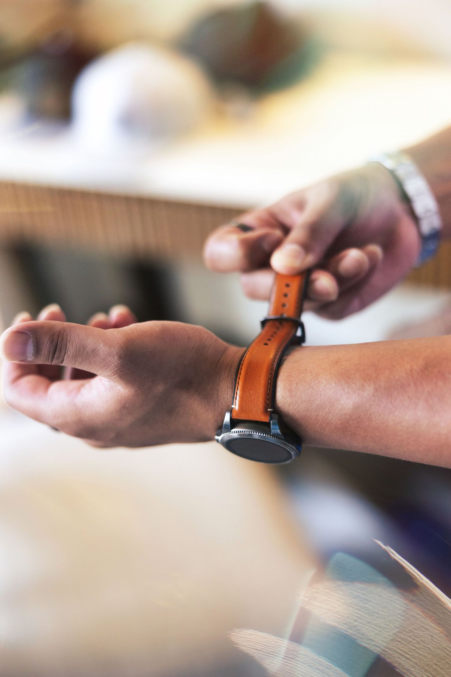 Close-up view of hands adjusting a brown leather smartwatch band on someone's wrist.