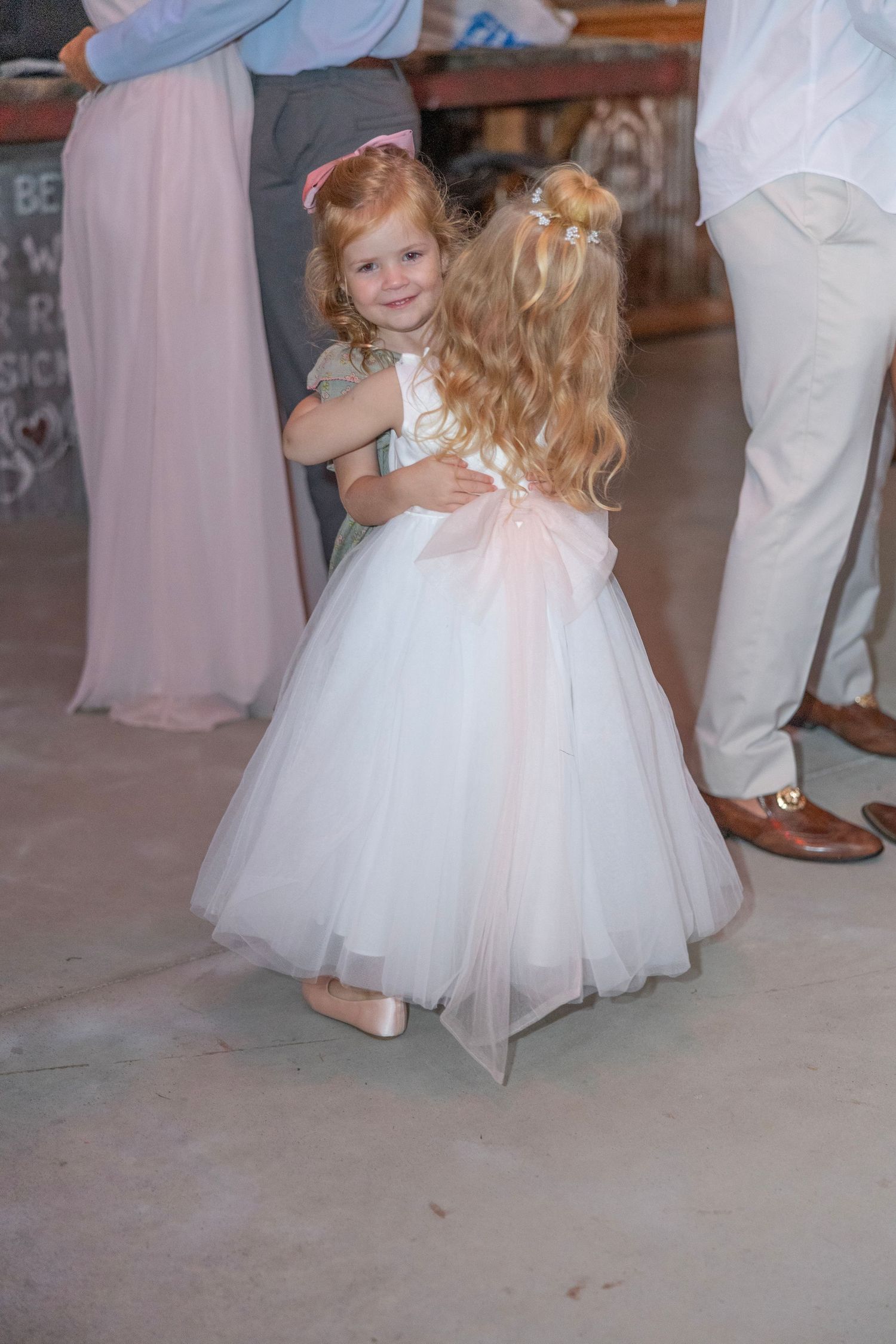 A flower girl in a white tulle dress twirls on the dance floor at a wedding reception.