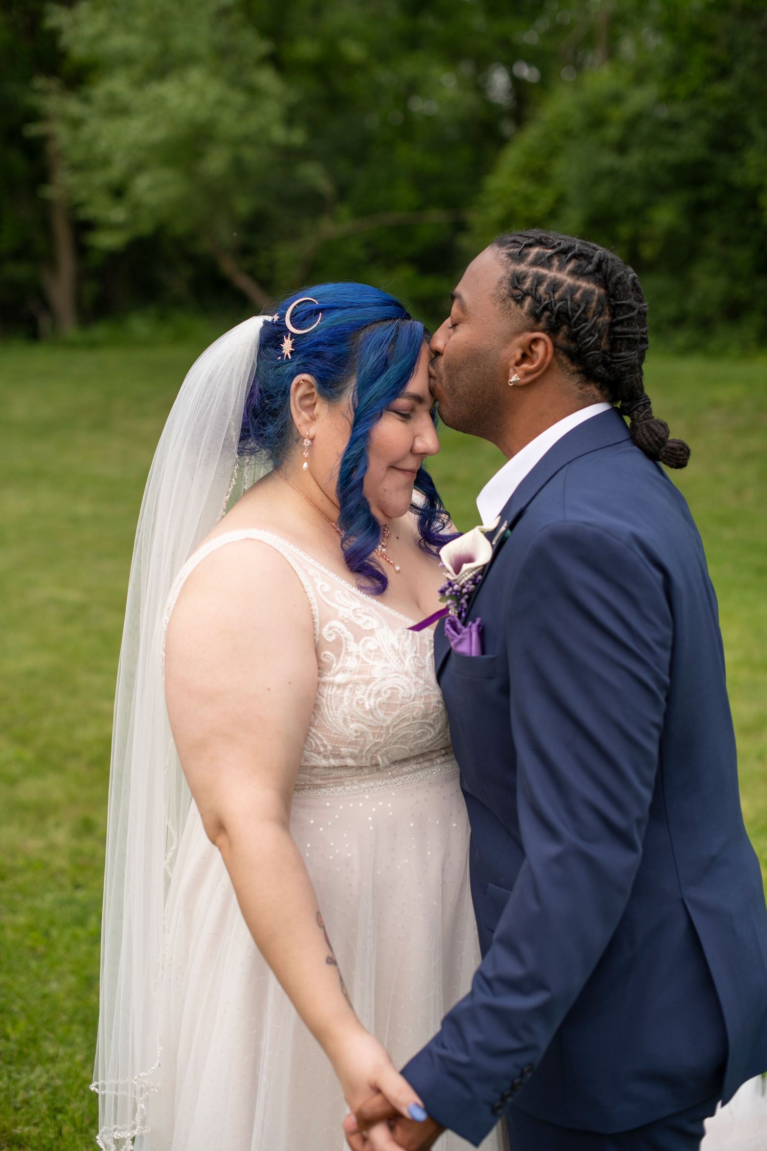 A couple shares an intimate kiss during their outdoor wedding ceremony while wearing navy and white attire.