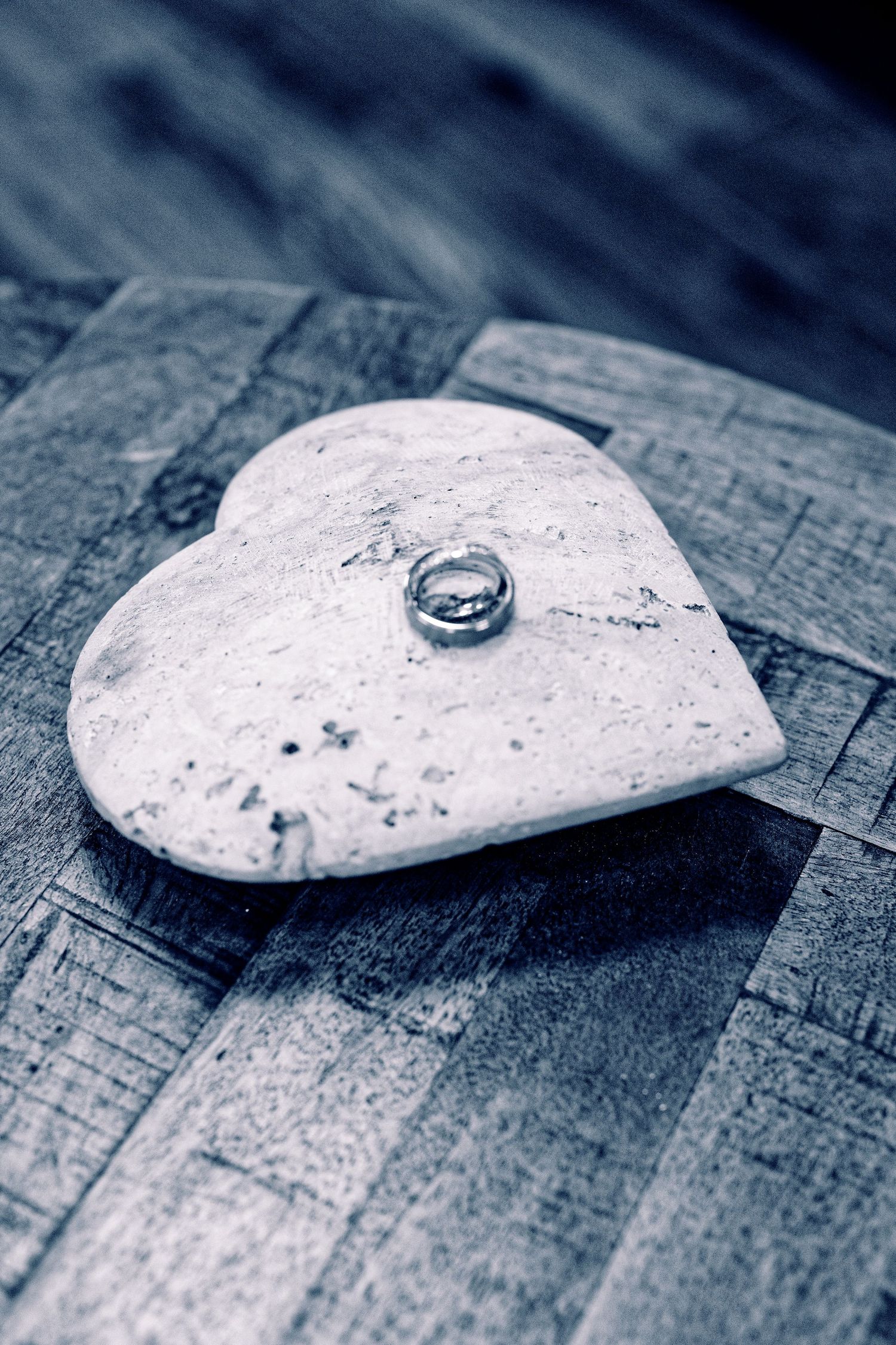 A silver wedding ring rests on a white heart-shaped stone against a rustic wooden surface.