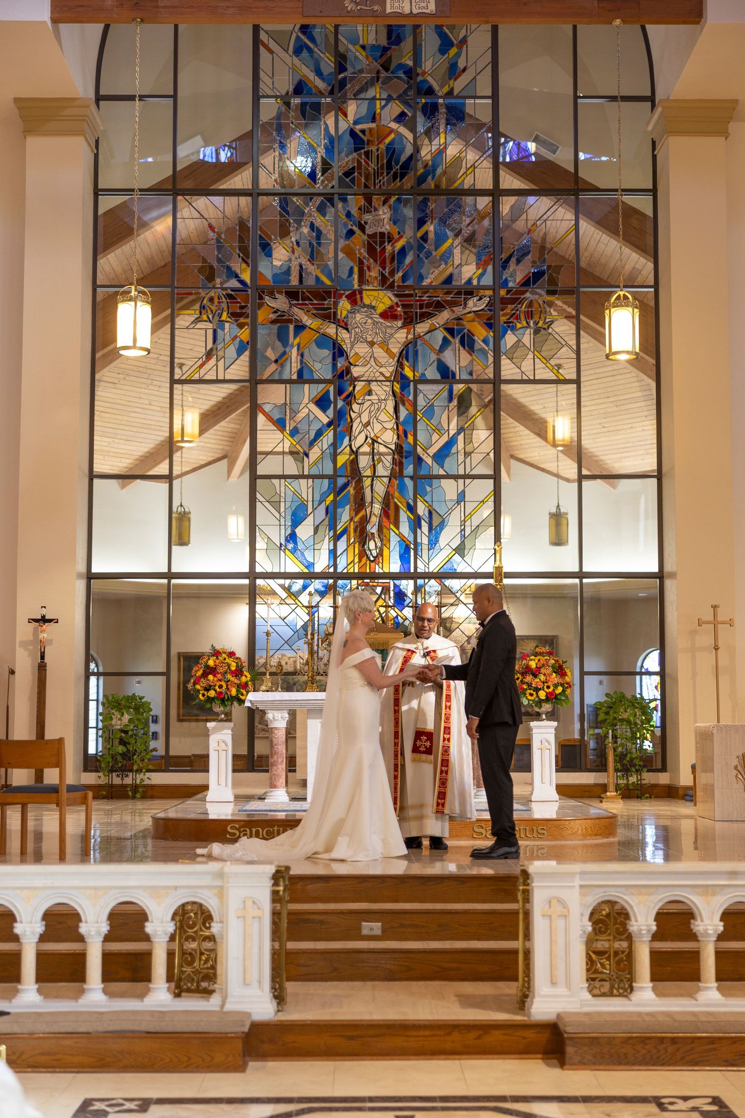 Wedding ceremony in modern church interior with stained glass windows and white columns during a traditional service.
