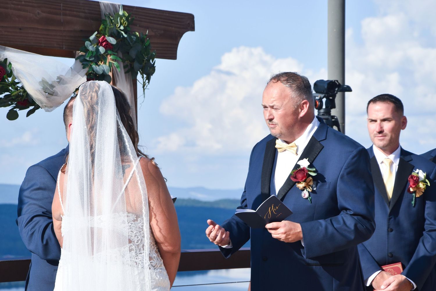 A couple exchanges rings during a waterfront wedding ceremony with blue ocean views in the background.