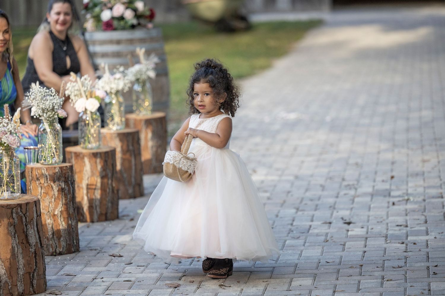 A person in a white wedding dress poses for photos on a stone pathway while holding a bouquet of flowers.