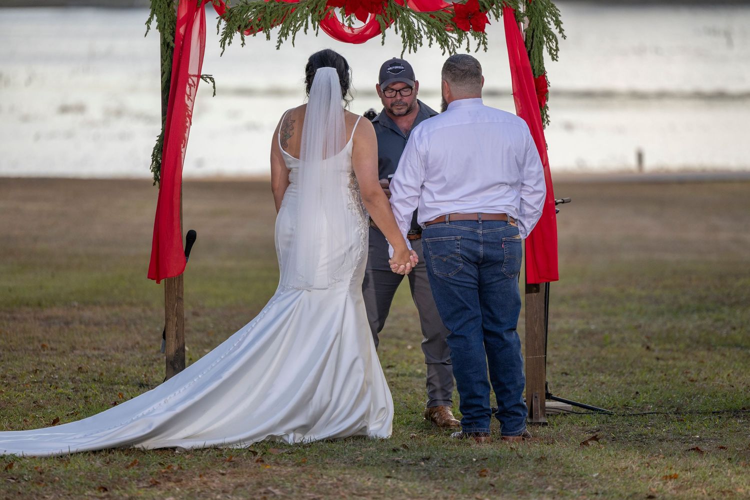 A couple in wedding attire poses for a series of romantic photos in an outdoor field setting with red decorative ribbons.