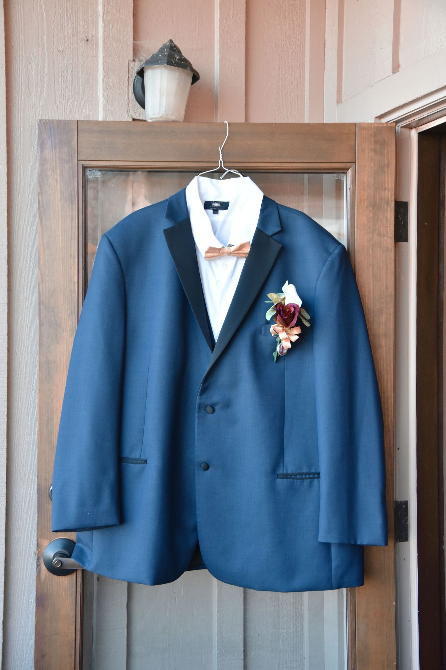 Row of navy blue groomsmen suits hanging on wooden wall with white boutonniere flowers.