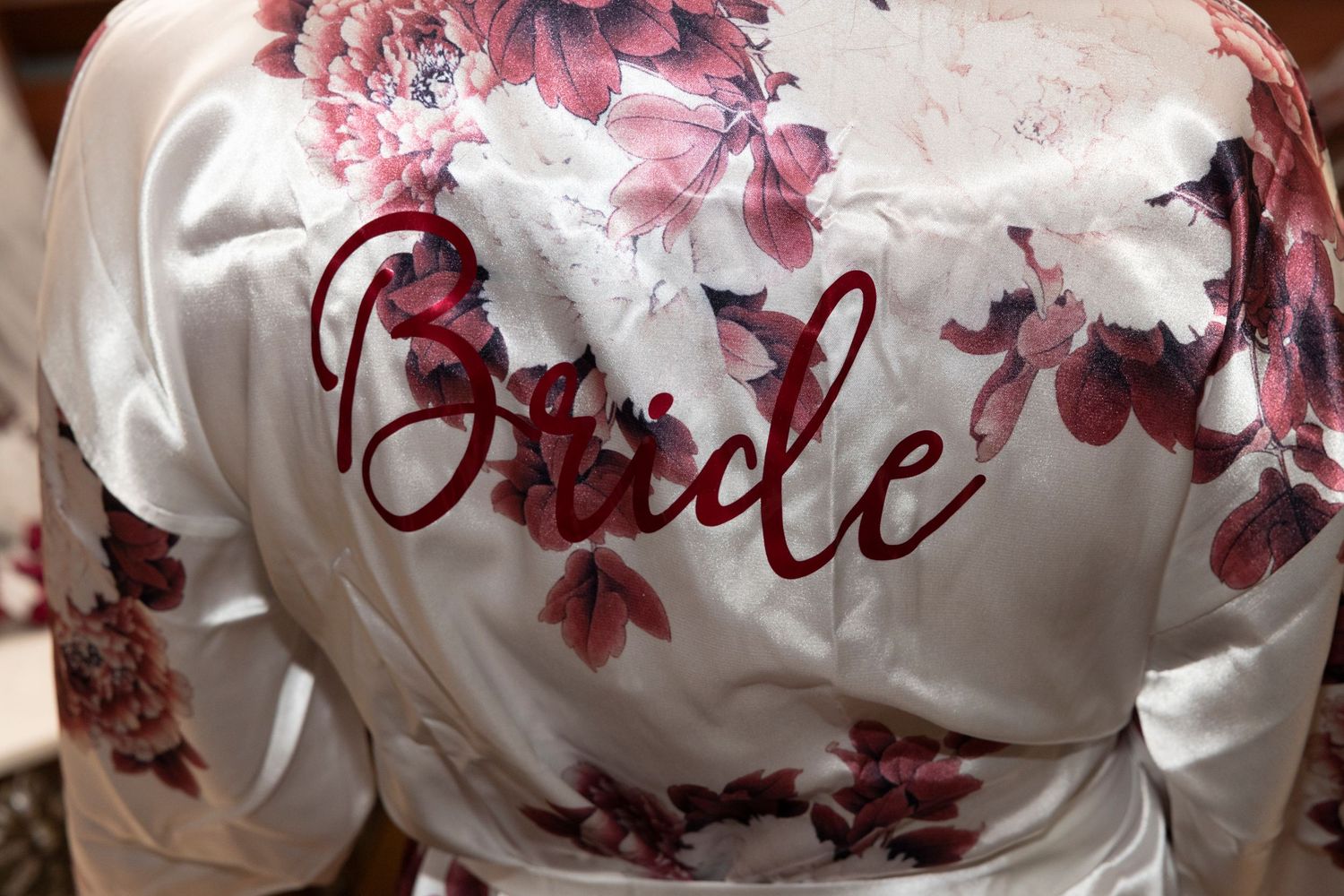 White silk robe with 'Bride' text in burgundy script and floral design, featuring delicate lace details.