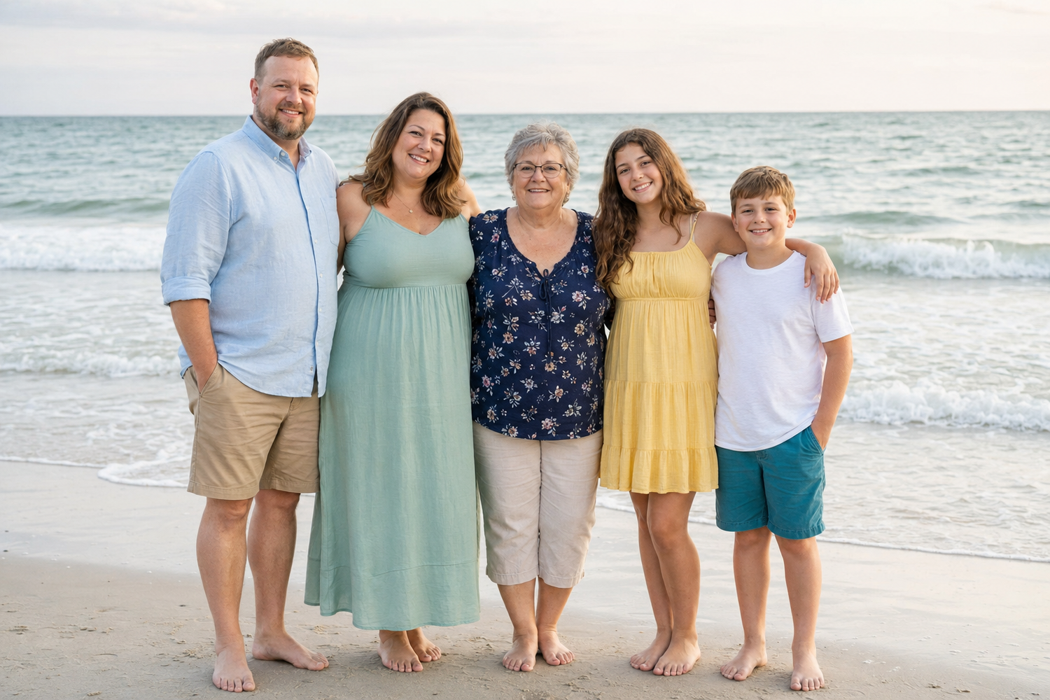 Family of five smiling together on a sandy beach with ocean waves in the background.