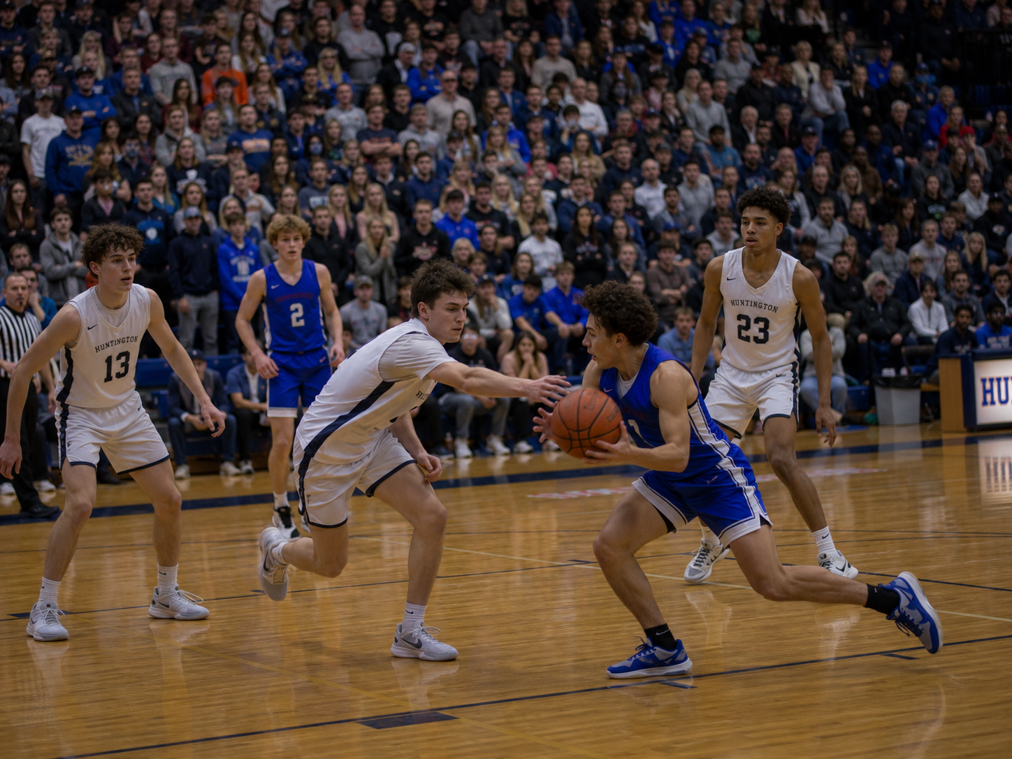 High school basketball players compete in a packed gym, with a defender reaching for the ball against a blue-uniformed opponent.