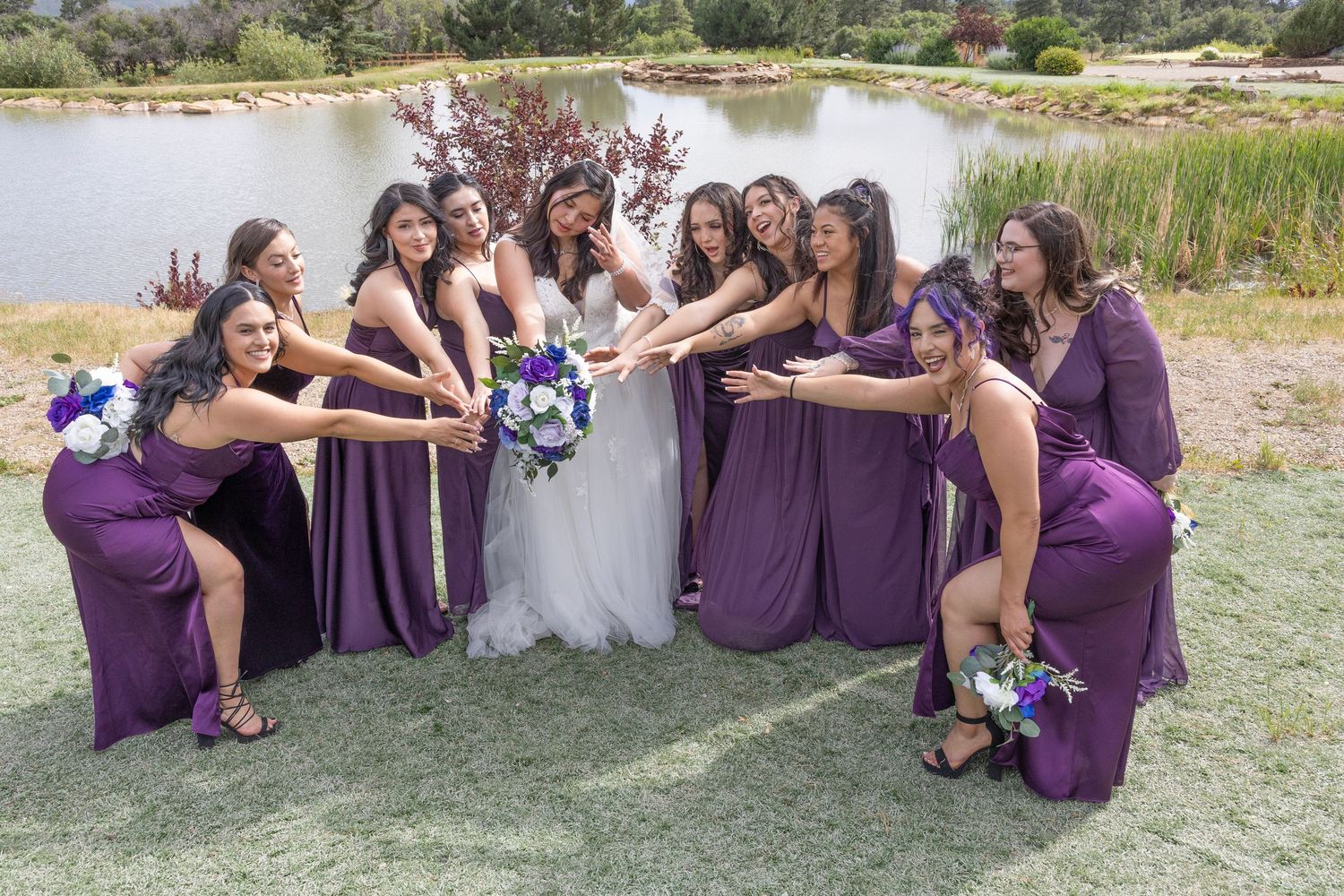 Wedding party in purple dresses sits together outdoors on a sunny day.