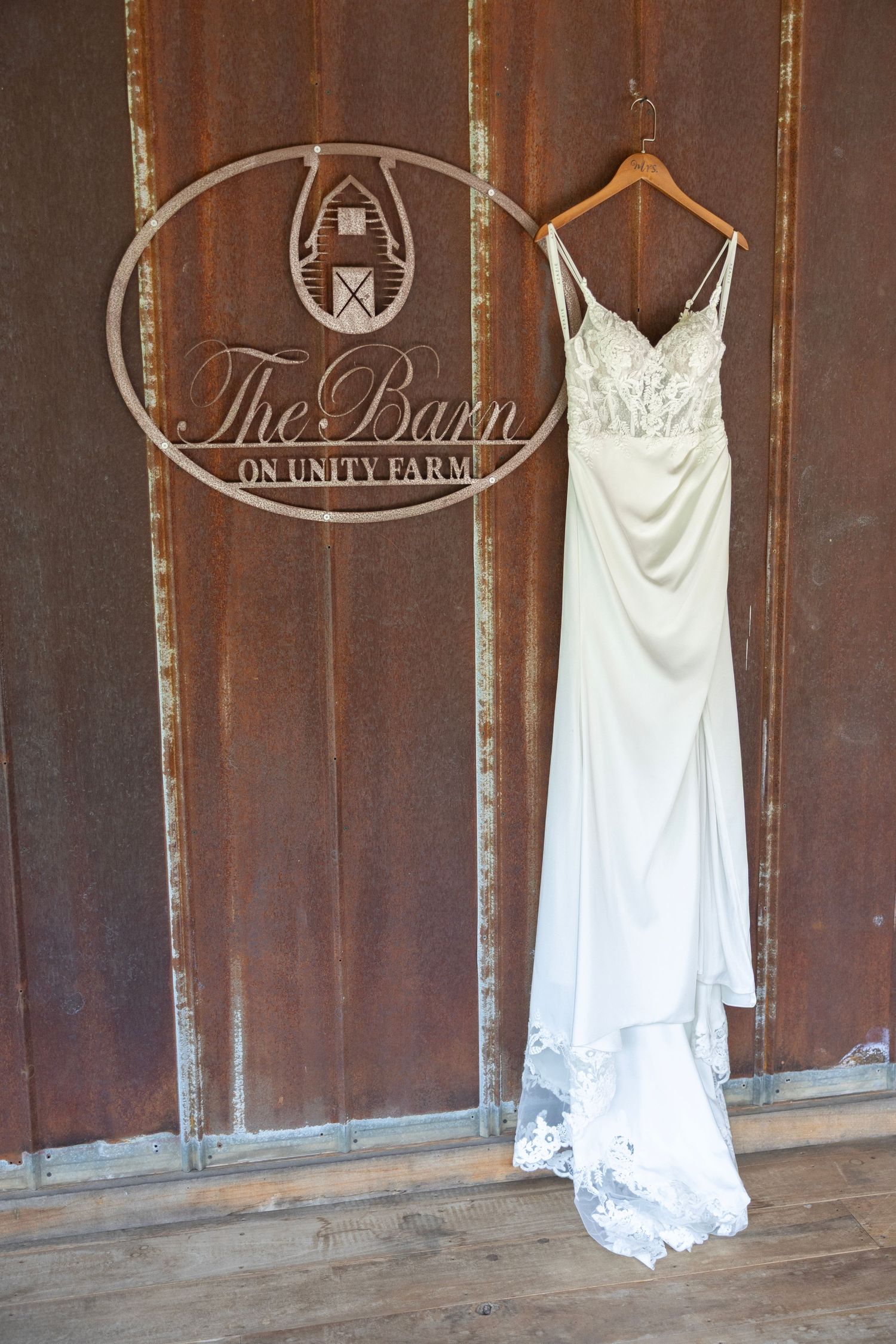 White wedding dresses hang on rustic wooden walls inside a barn venue with elegant signage.