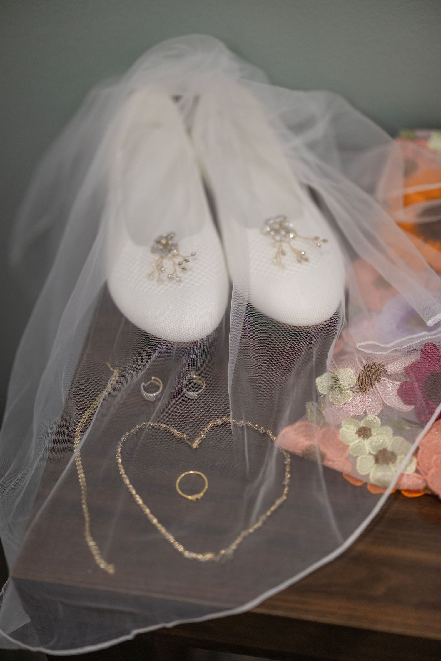 Wedding accessories including white slippers, veil, and delicate jewelry arranged on a dark wooden surface.