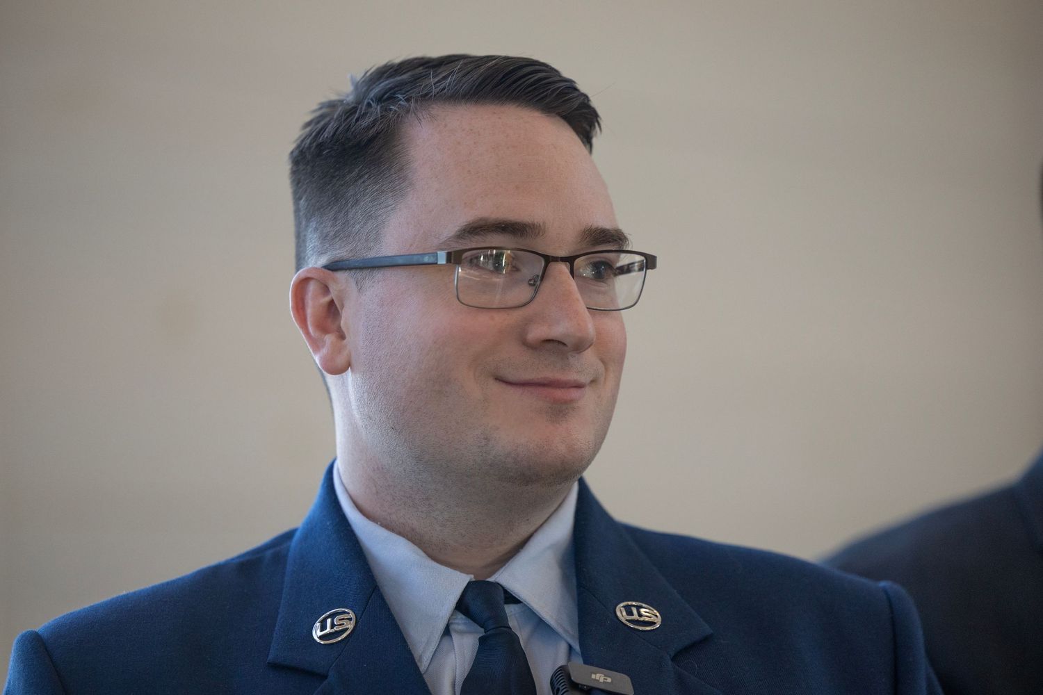 A person in Air Force military uniform wearing glasses smiles warmly at the camera.