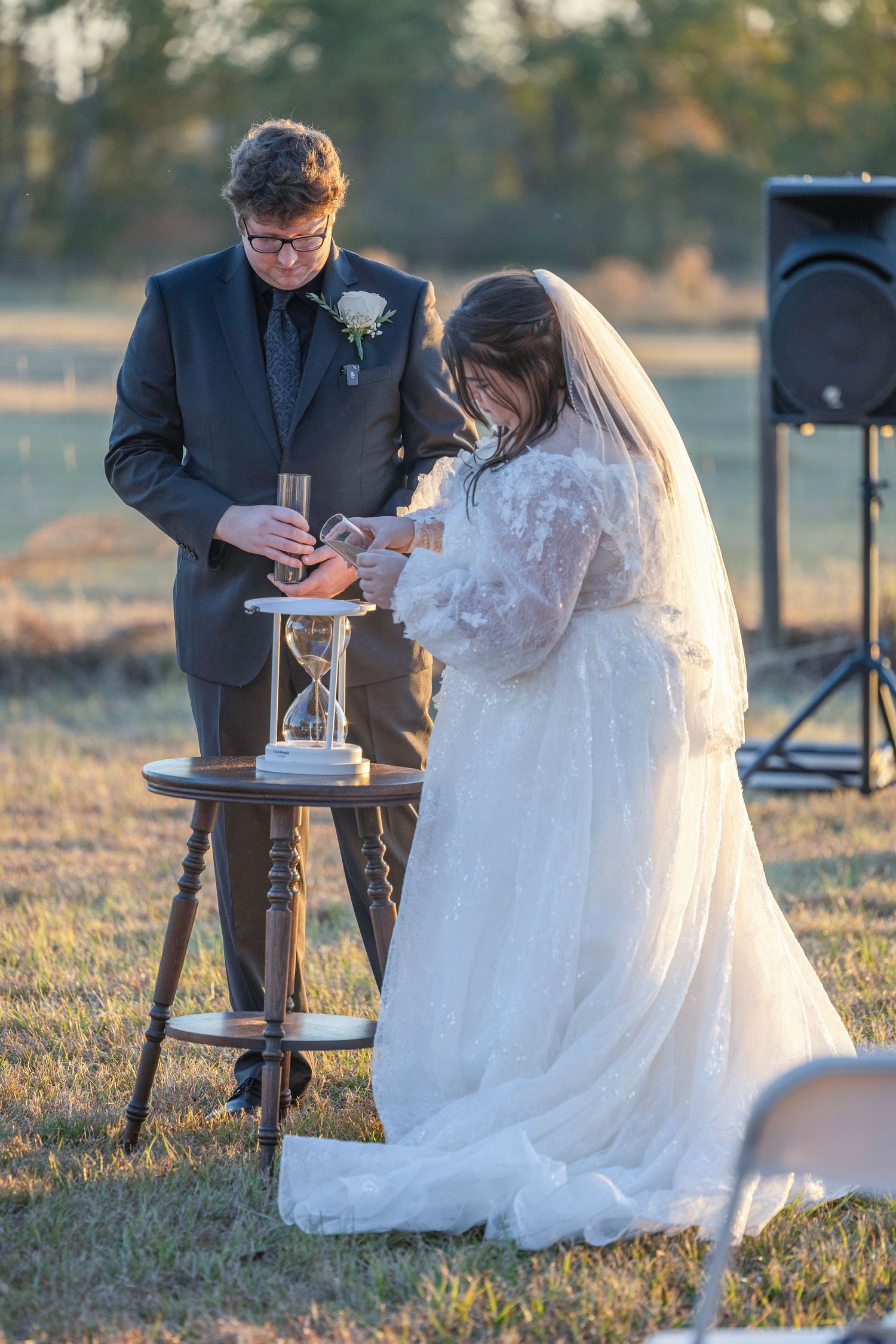 A couple performs a unity ceremony at their outdoor wedding during golden hour sunset.