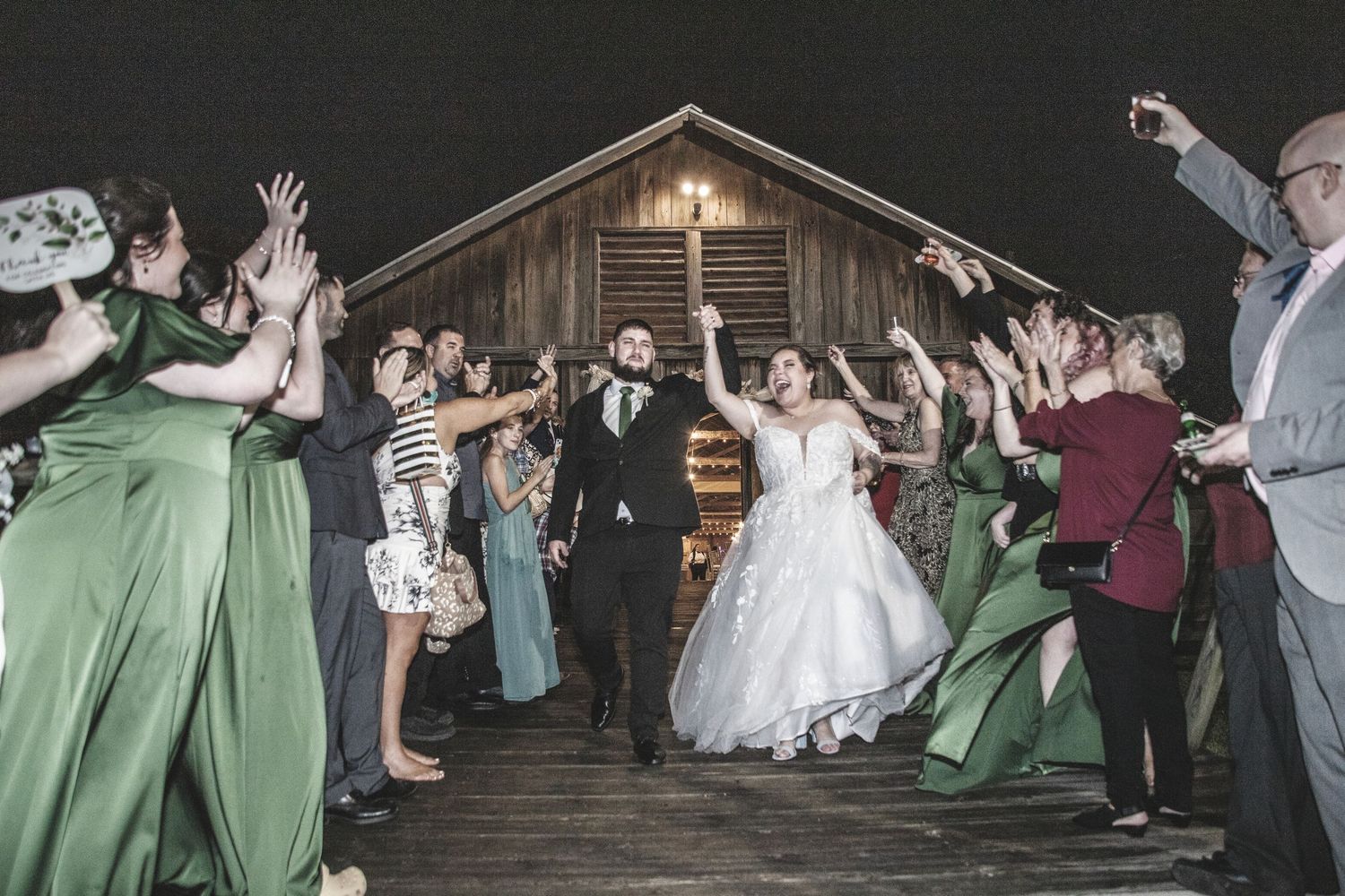 Wedding guests form a tunnel with raised arms for the newlyweds to walk through during an evening reception celebration.