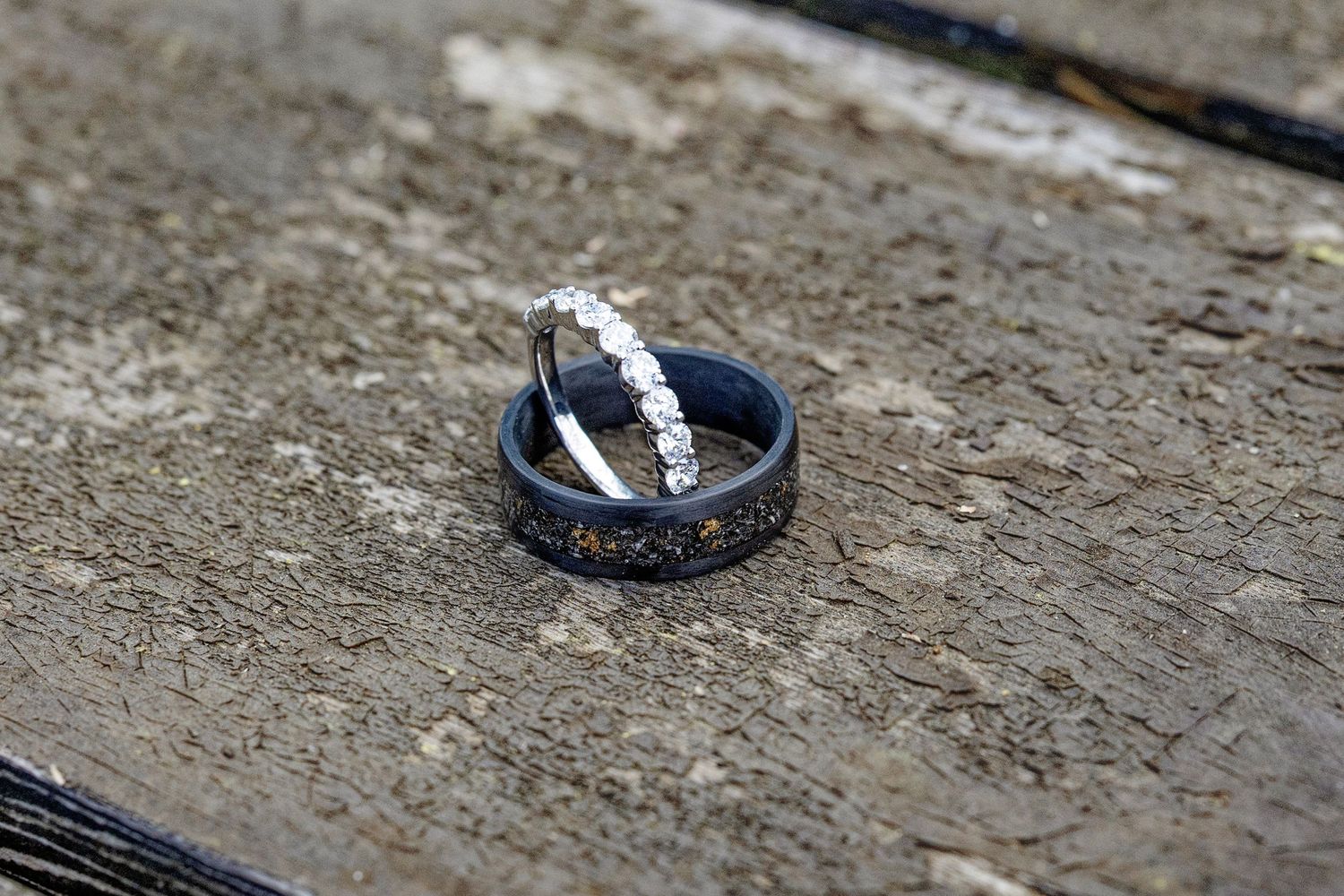 Two wedding rings on a wooden surface, featuring a diamond eternity band and a black ring with gold meteorite inlay.