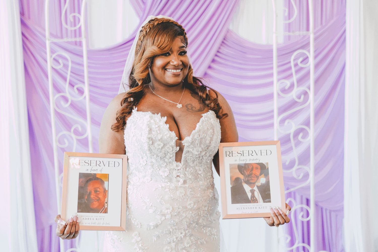 Bride in lace mermaid wedding gown holding two framed magazine covers at elegant lavender draped ceremony backdrop.