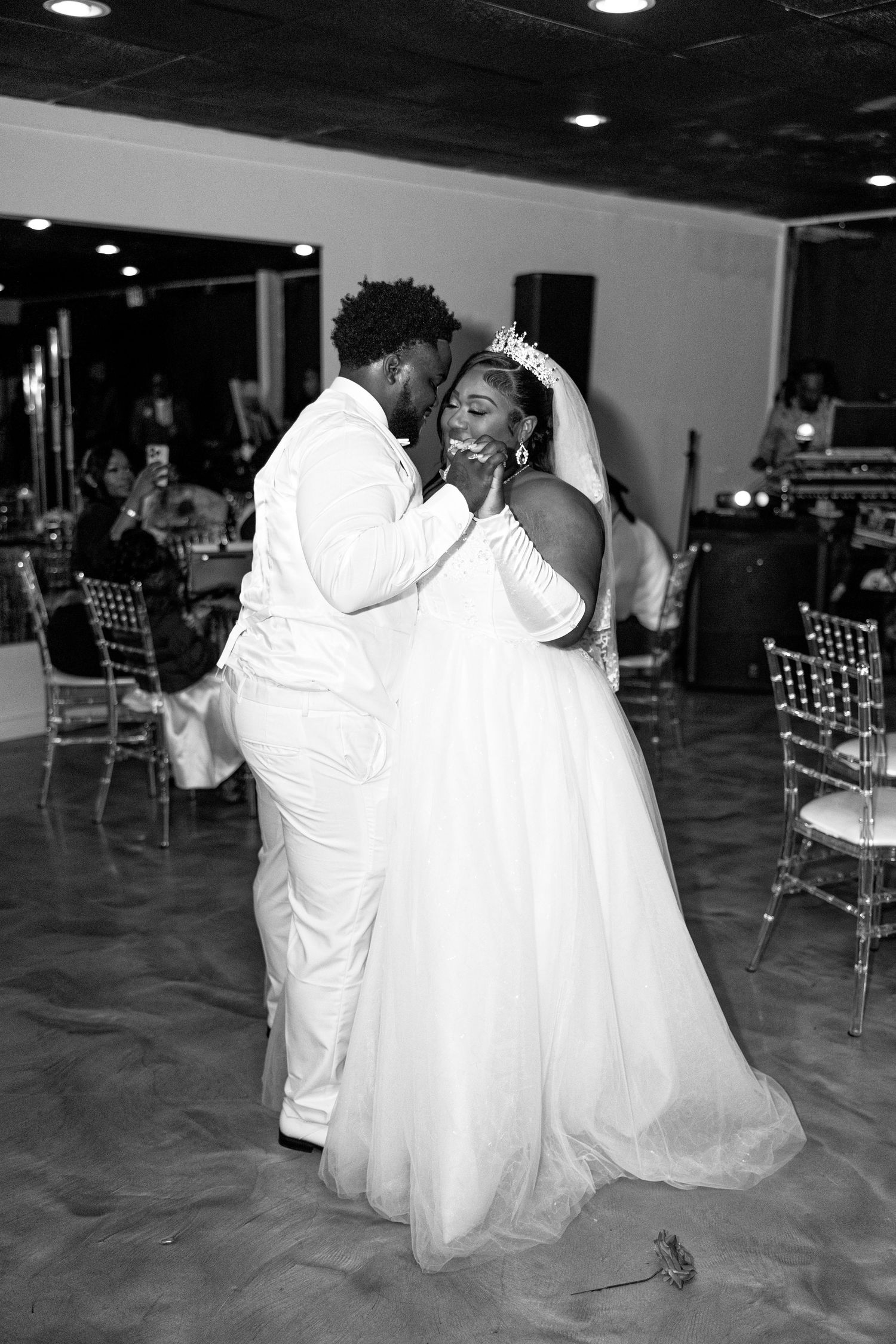 Black and white photo of a bride and groom sharing their first dance at a wedding reception.