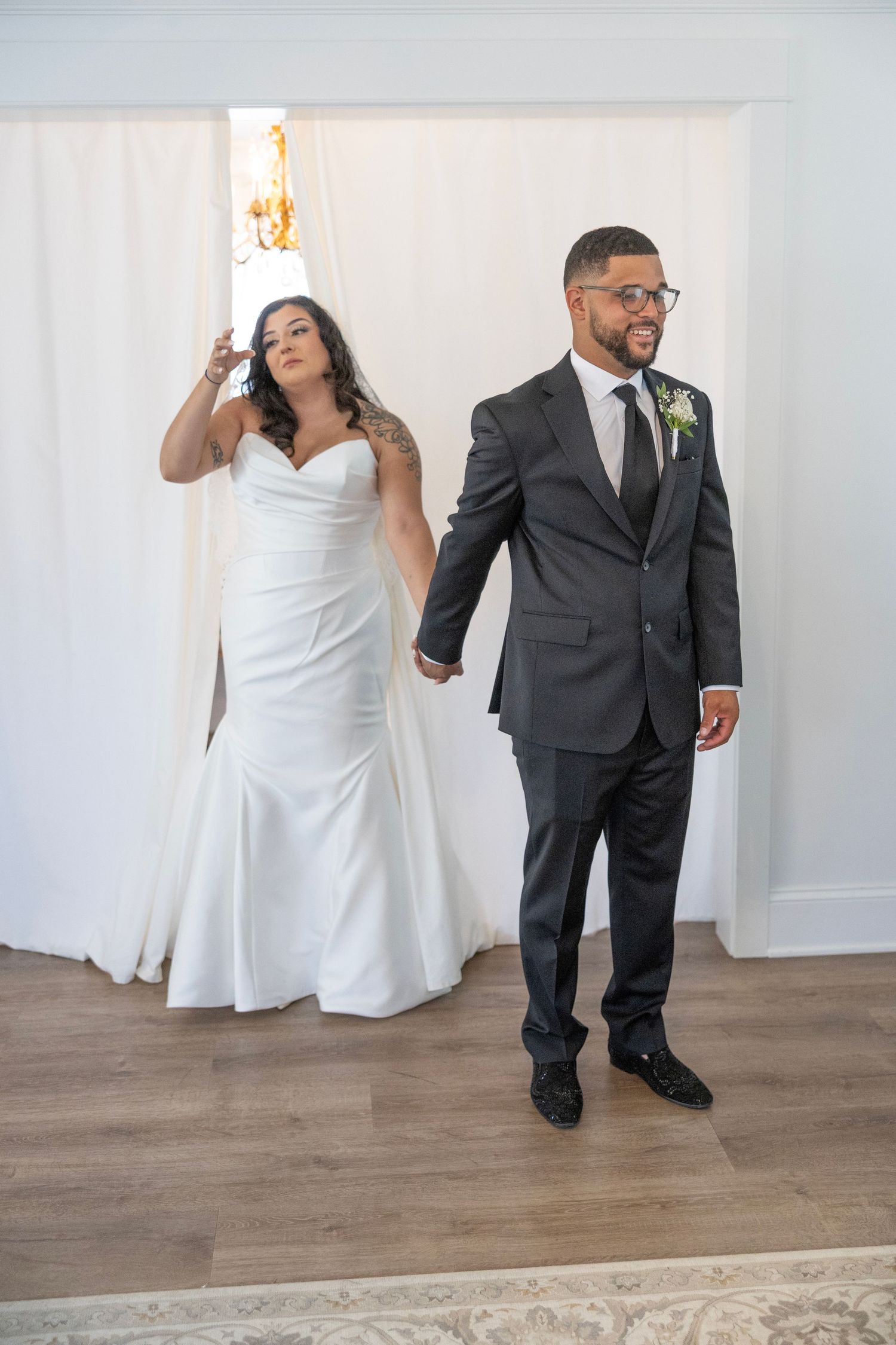 Bride in white dress and groom in dark suit dance playfully together on wooden floors during their wedding celebration.