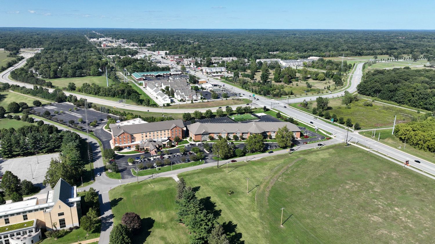 Aerial panoramic view of a coastal town showing roads, buildings, and green spaces stretching along the shoreline.
