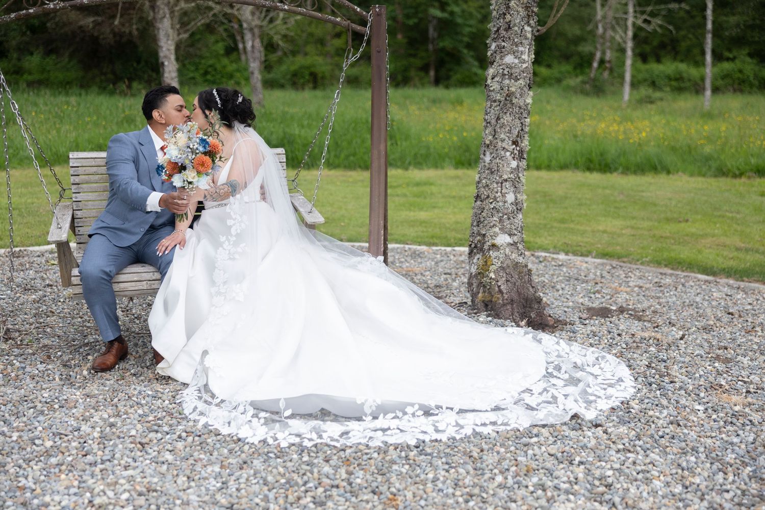 A romantic wedding scene unfolds in a rustic outdoor setting with birch trees and gravel path.