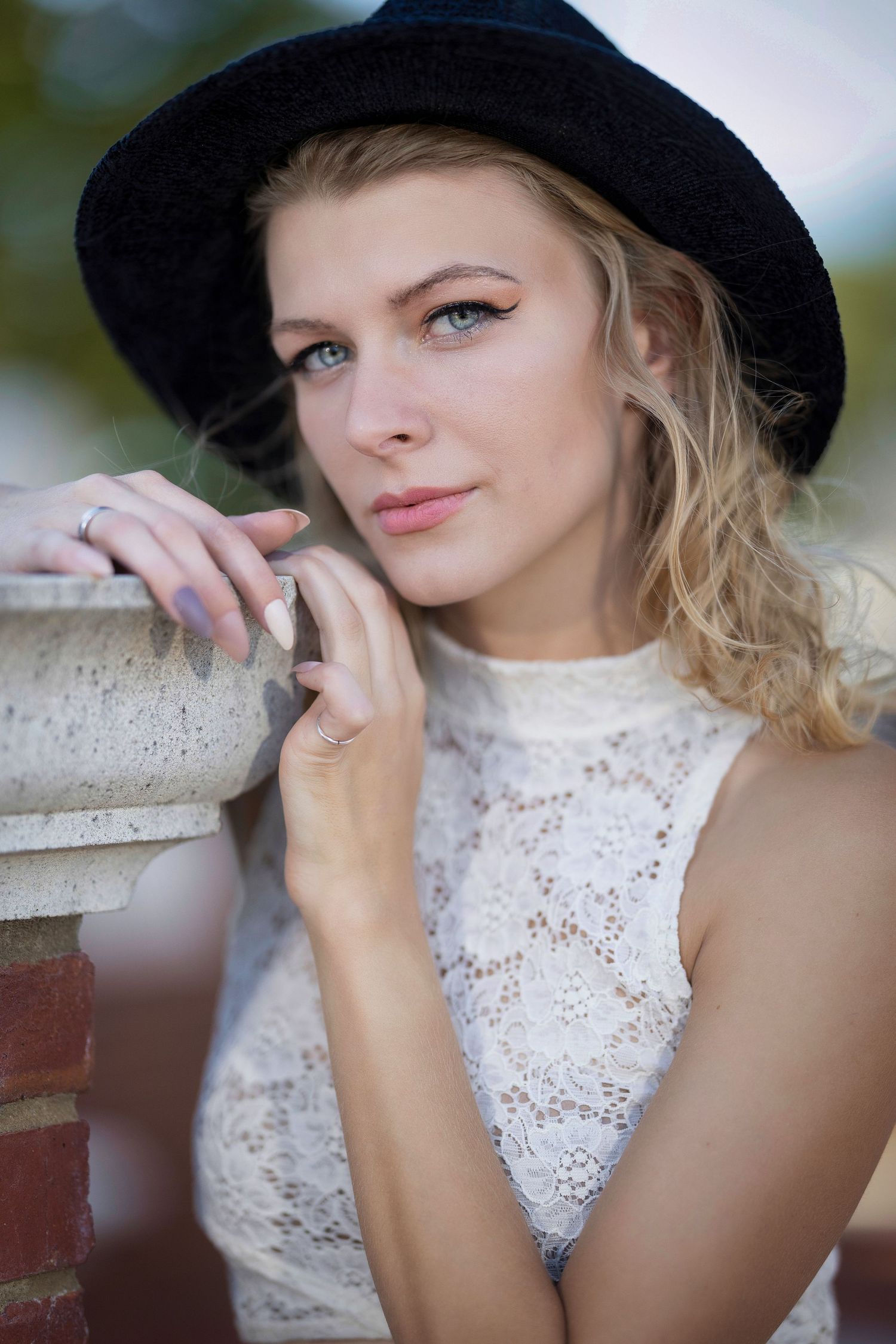 A series of artistic portrait shots showing someone in a black hat and white lace top posing against a light background.
