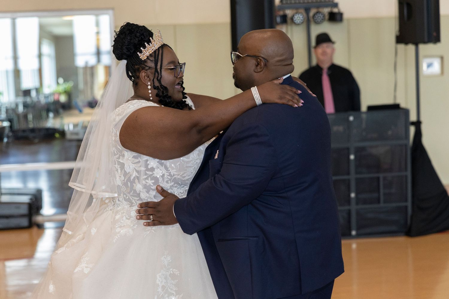 Bride and groom share their first dance at wedding reception, wearing white gown and navy suit.