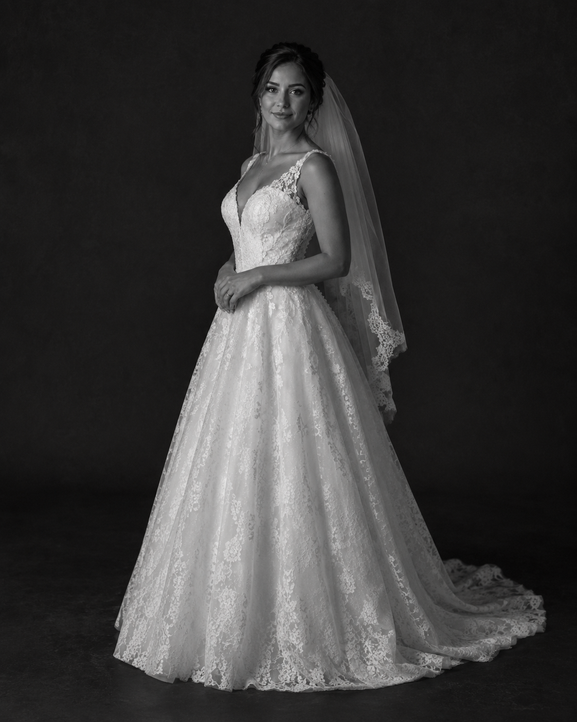 Bride in elegant lace ball gown wedding dress with veil, posing in black and white portrait photo.