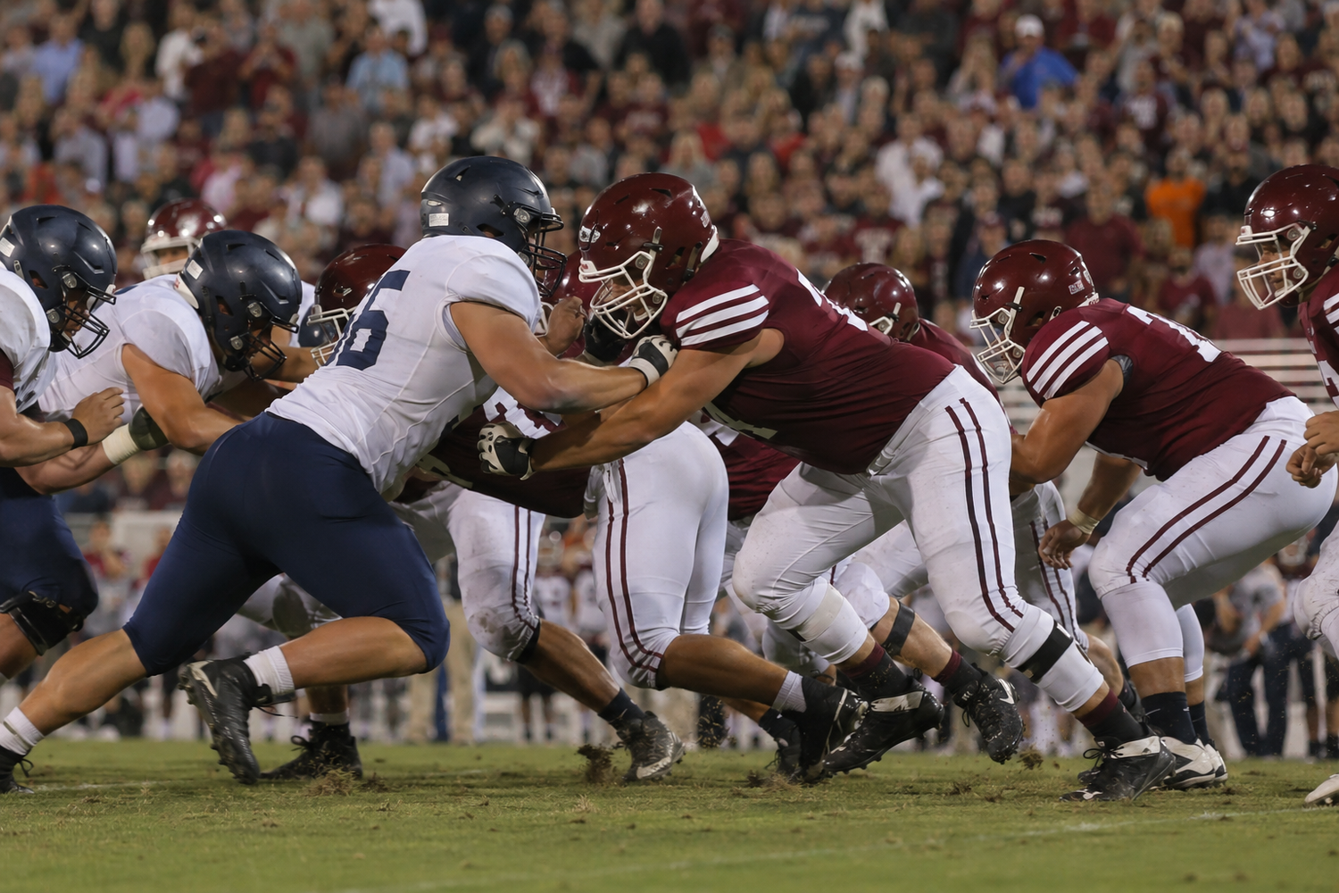 Football linemen clash at the line of scrimmage during a college football game at night.