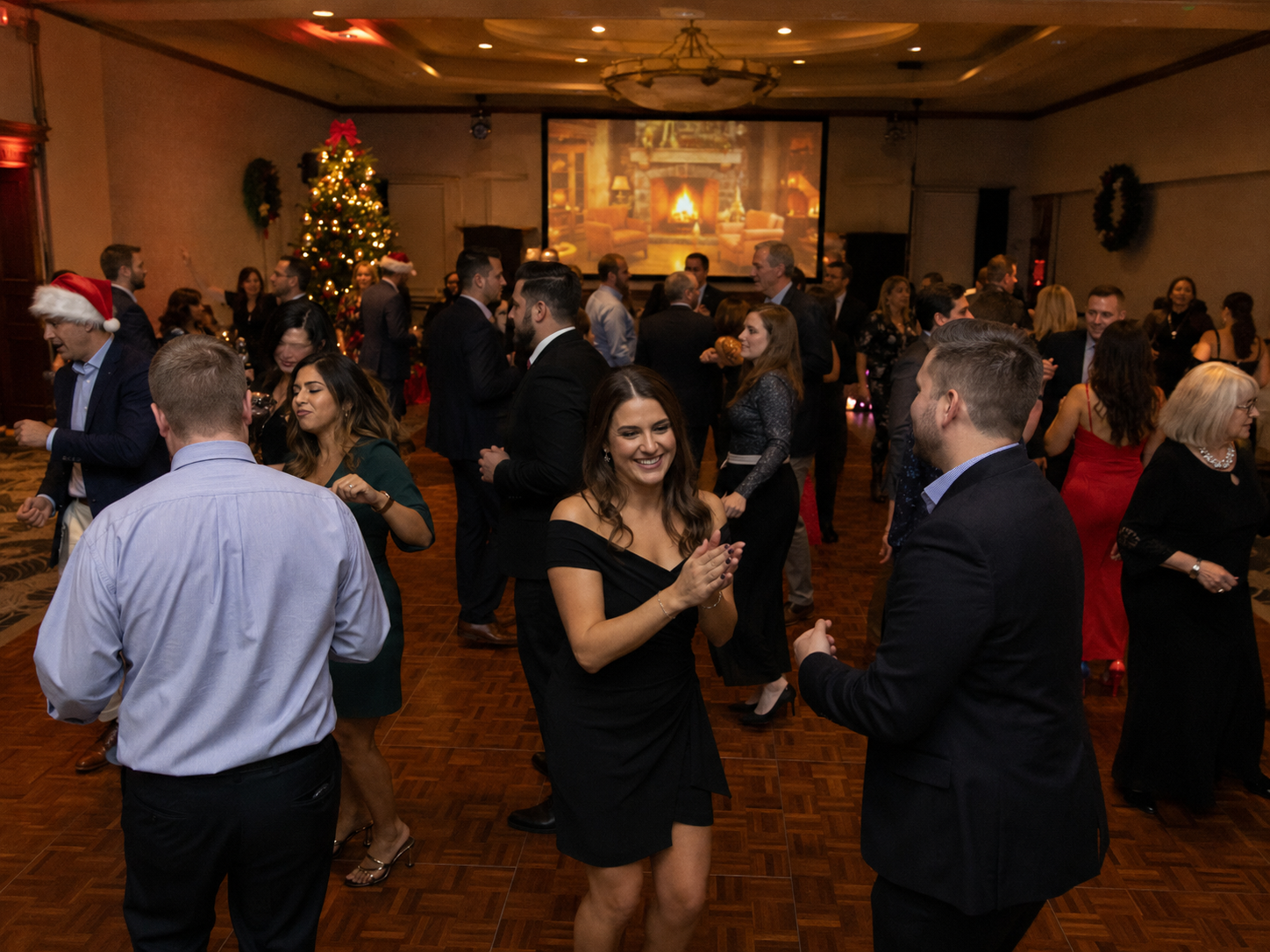 Elegantly dressed guests dancing and socializing at a festive Christmas holiday party with decorated tree.