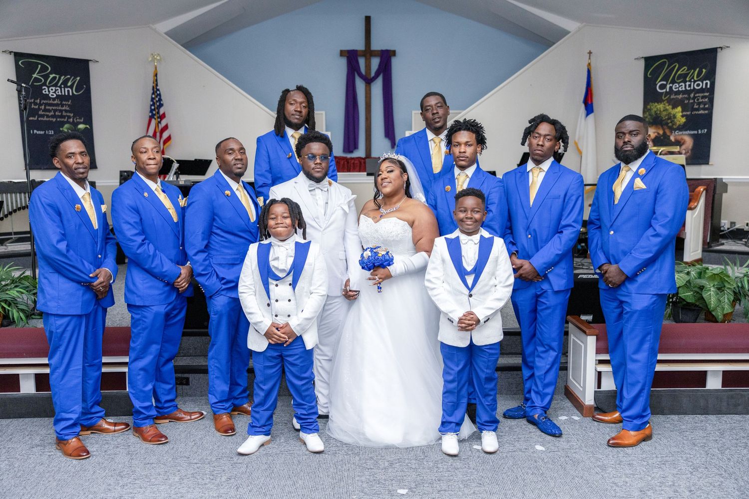 Wedding party poses in church with groomsmen in royal blue suits and bride and groom in white attire.