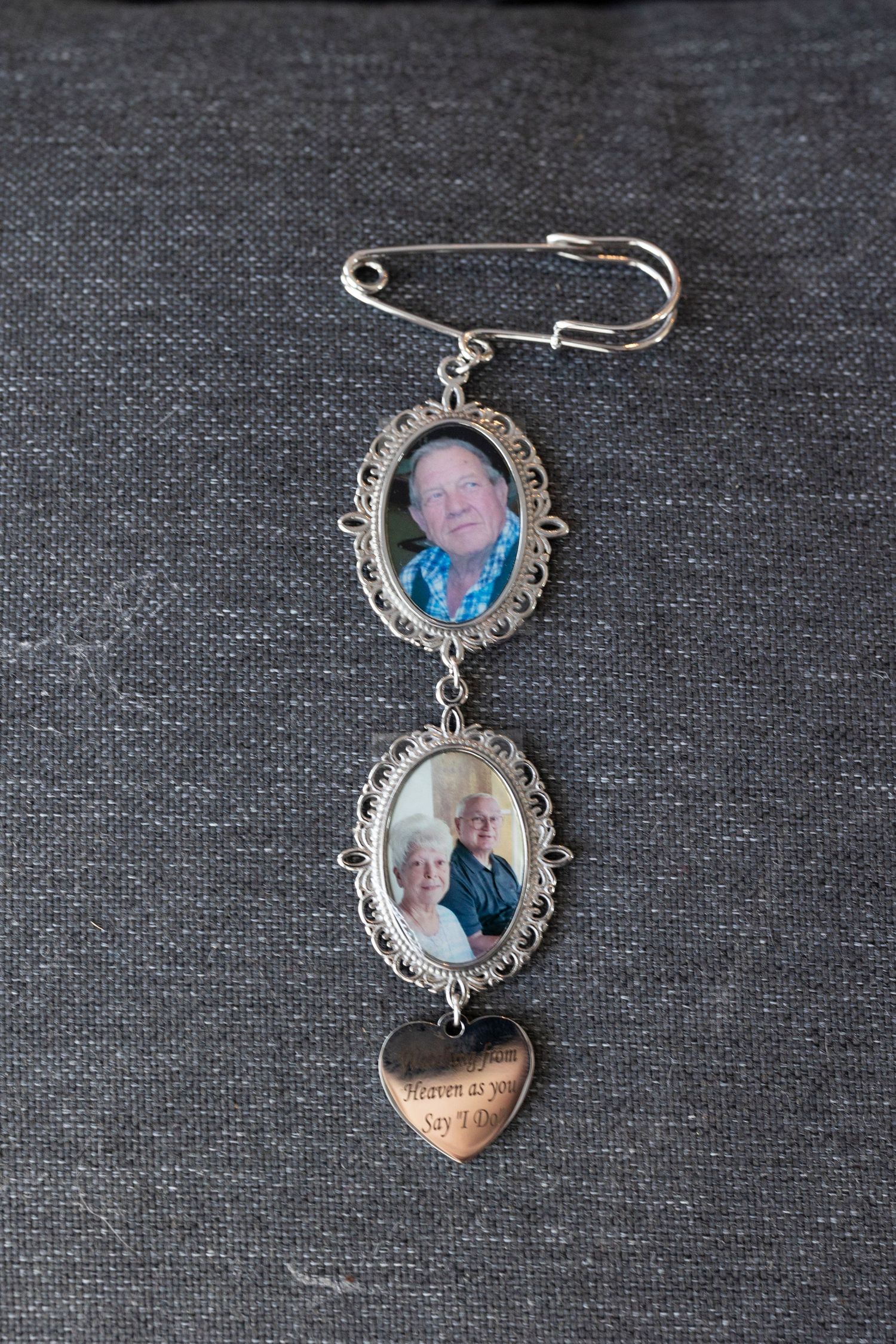 Vintage-style silver brooch pin with two oval photo frames and a decorative heart charm on gray fabric.