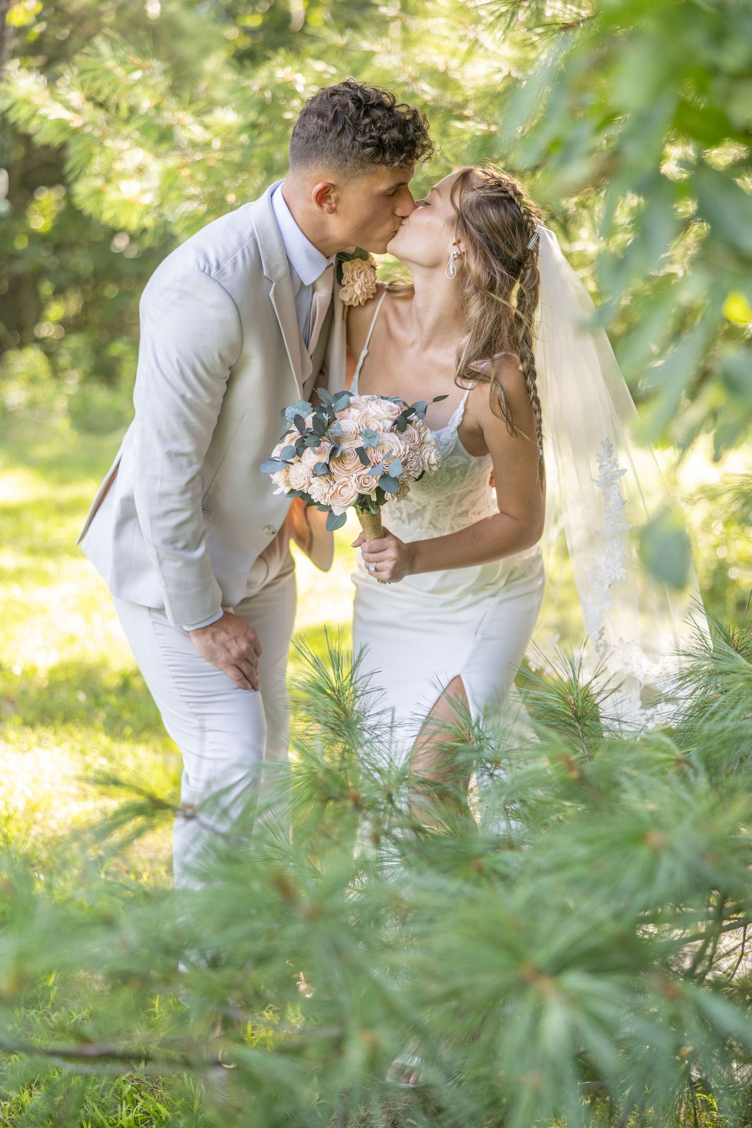 Romantic wedding couple embraces in a sunlit garden setting with lush greenery framing their tender moment.
