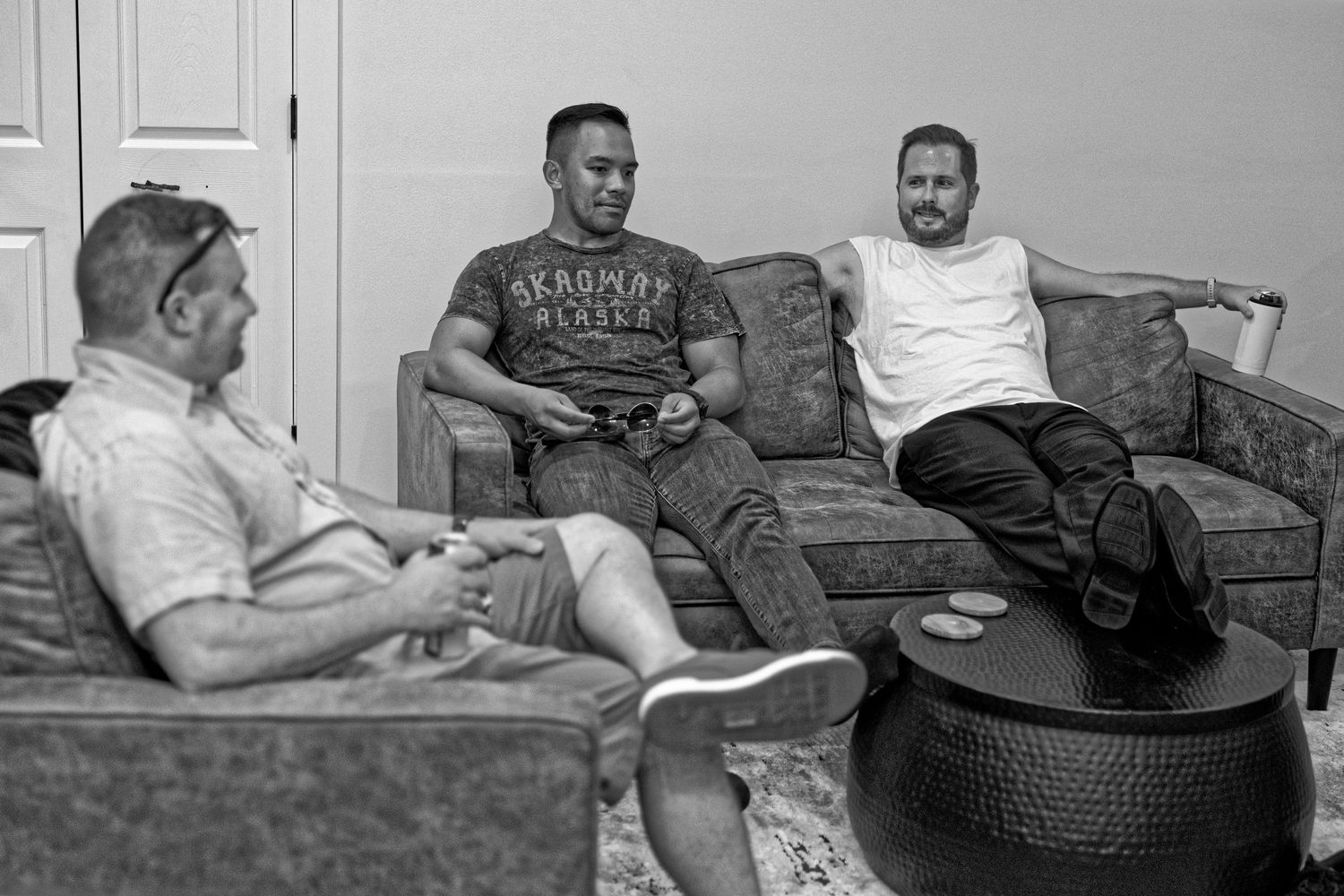 A vintage black and white photograph shows people relaxing in a living room setting with mid-century furniture.