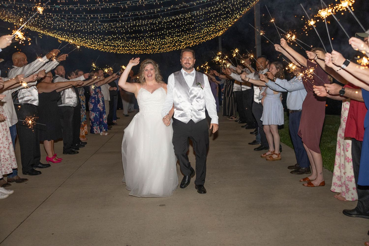 Wedding guests hold sparklers forming a glowing tunnel as newlyweds dance through during an evening reception celebration.