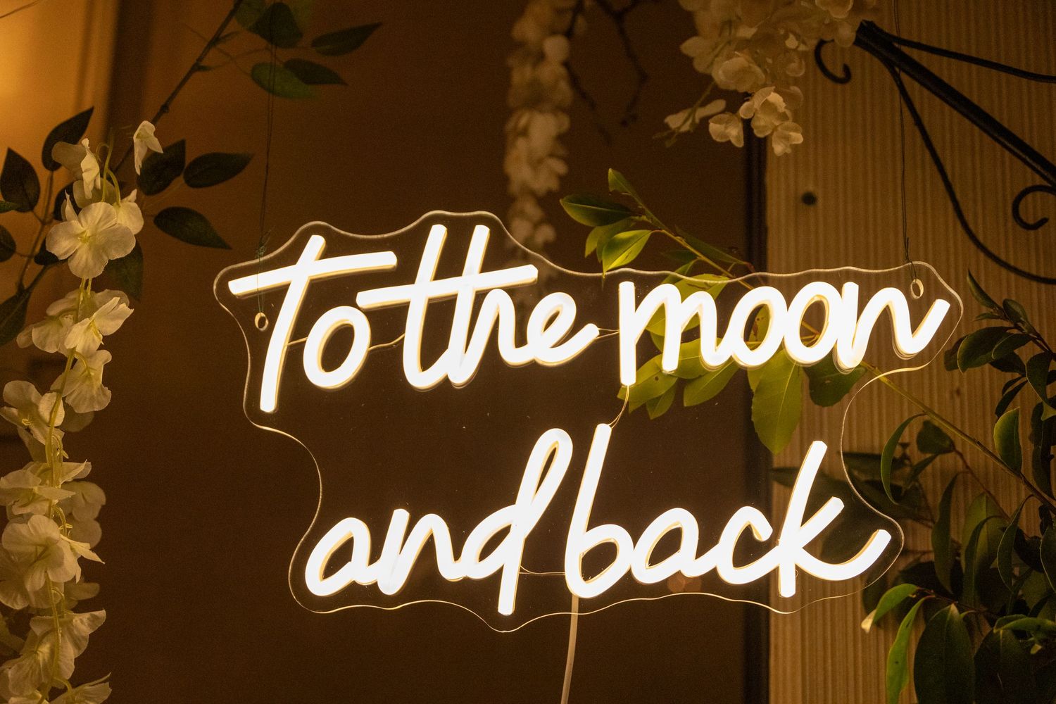 White neon sign reading 'to the moon and back' mounted on wall with decorative floral elements.