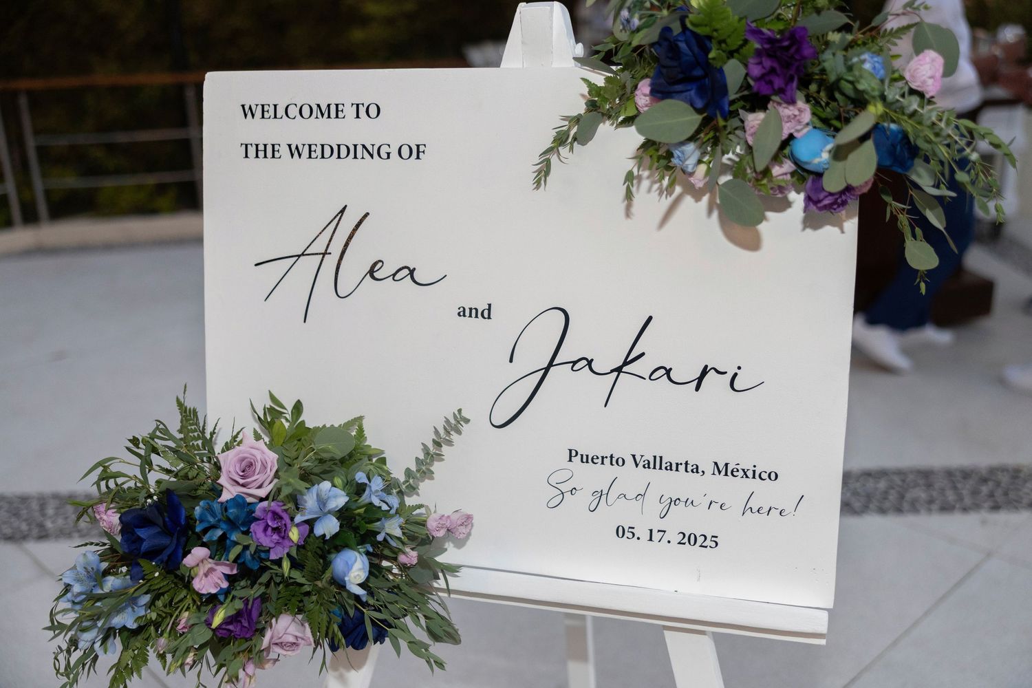 Elegant wedding welcome sign with calligraphy names displayed with blue and purple floral arrangements in Puerto Vallarta.