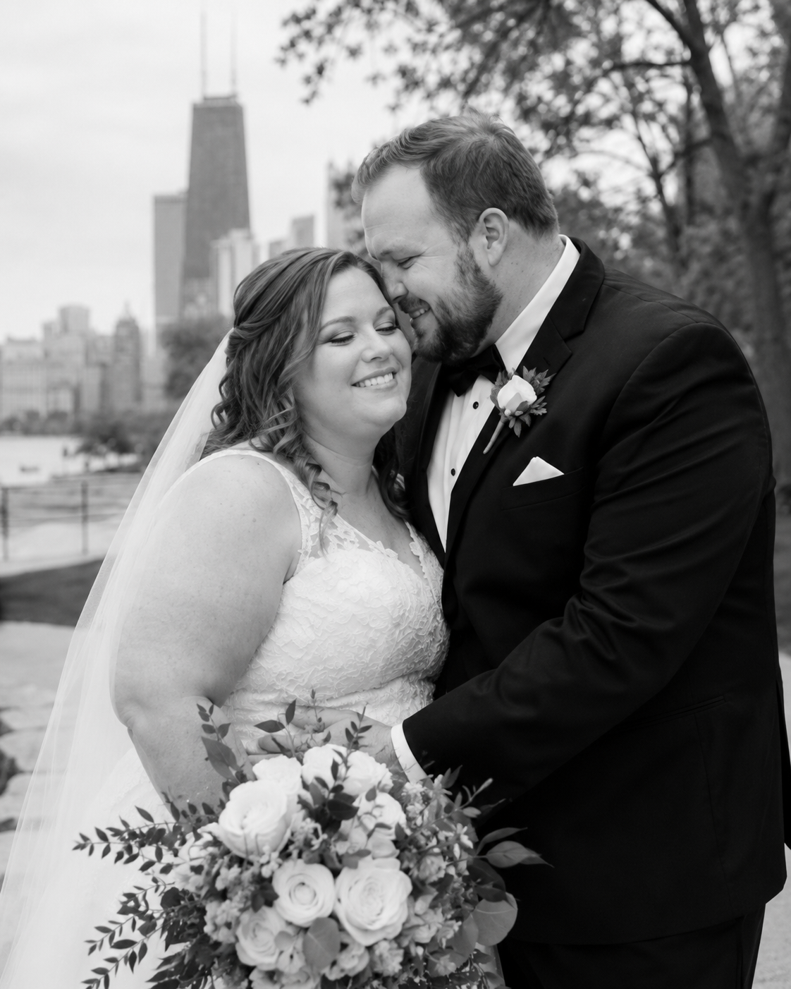 Black and white wedding portrait of bride and groom embracing with Chicago skyline in background.