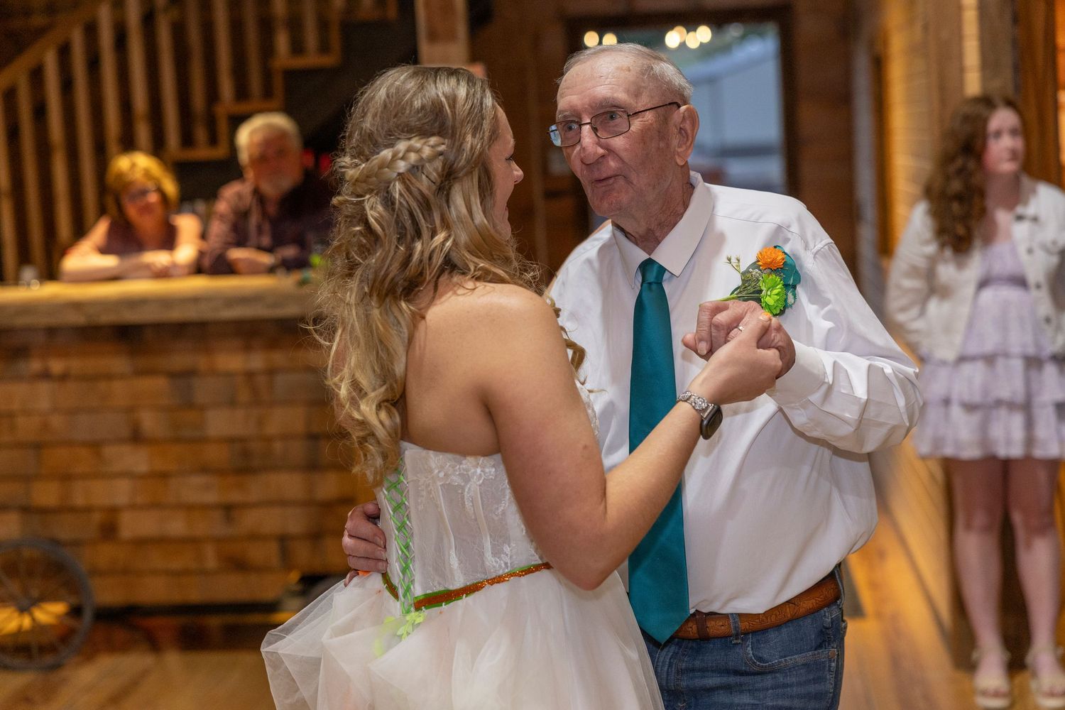 Bride and elderly man share a heartfelt father-daughter dance at a rustic barn wedding reception.