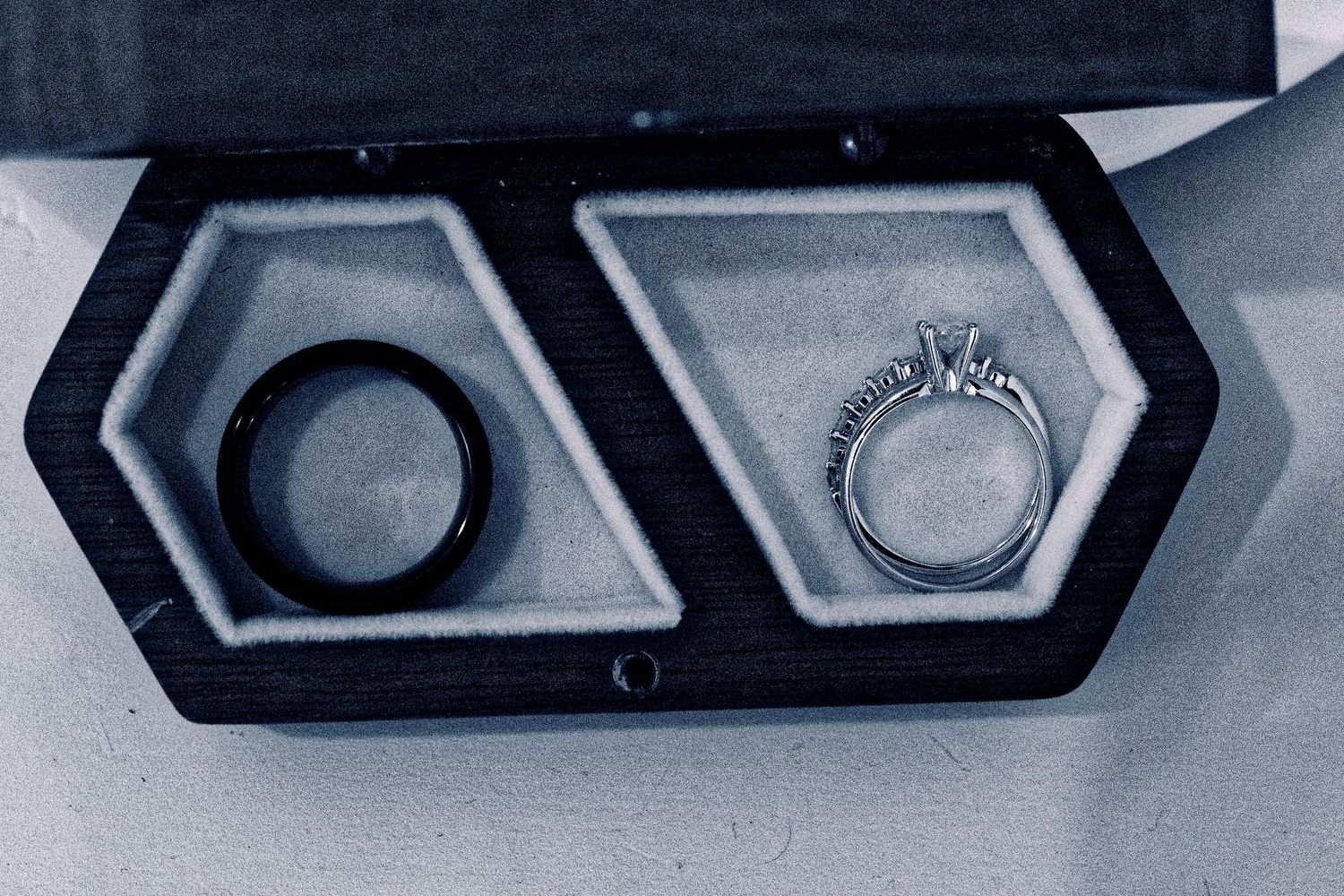 Two wedding rings displayed in a black velvet ring box, featuring a black tungsten band and a diamond engagement ring.