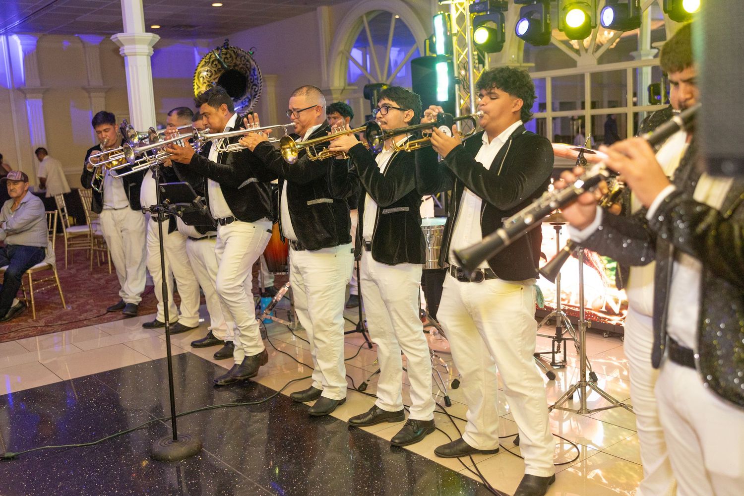 Brass band musicians in matching black and white uniforms perform on stage at an elegant indoor event venue.