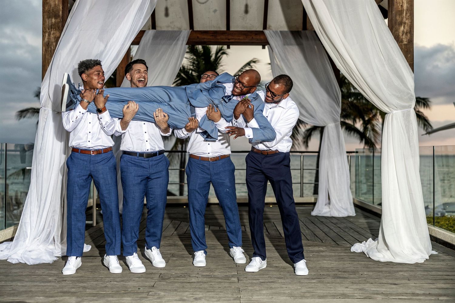 Group wearing matching blue pants and white shirts pose together under an elegant white draped canopy at an outdoor event.