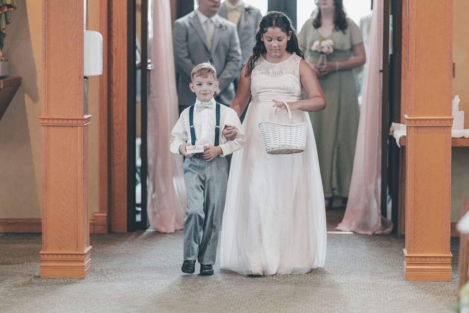 A group of people in formal attire gather in an elegant hallway with orange pillars and wooden doors.