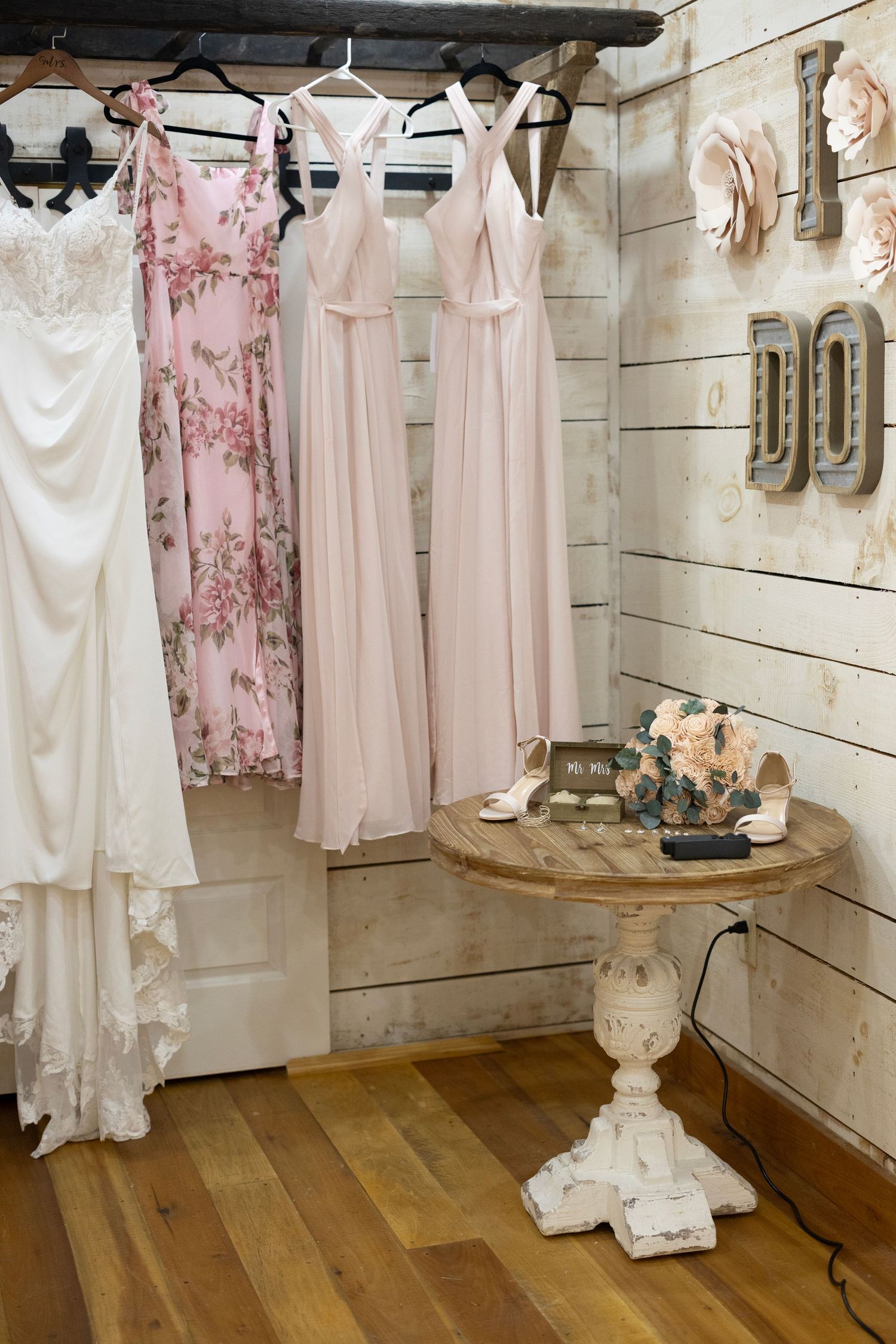 A collection of vintage-style white and pink dresses hanging on display in a rustic boutique with wooden floors.