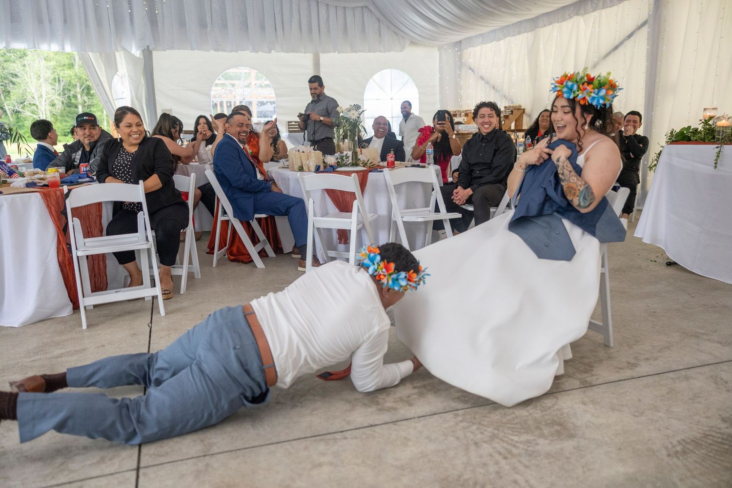 Wedding guests participate in a fun dance game at an outdoor reception under a white tent.